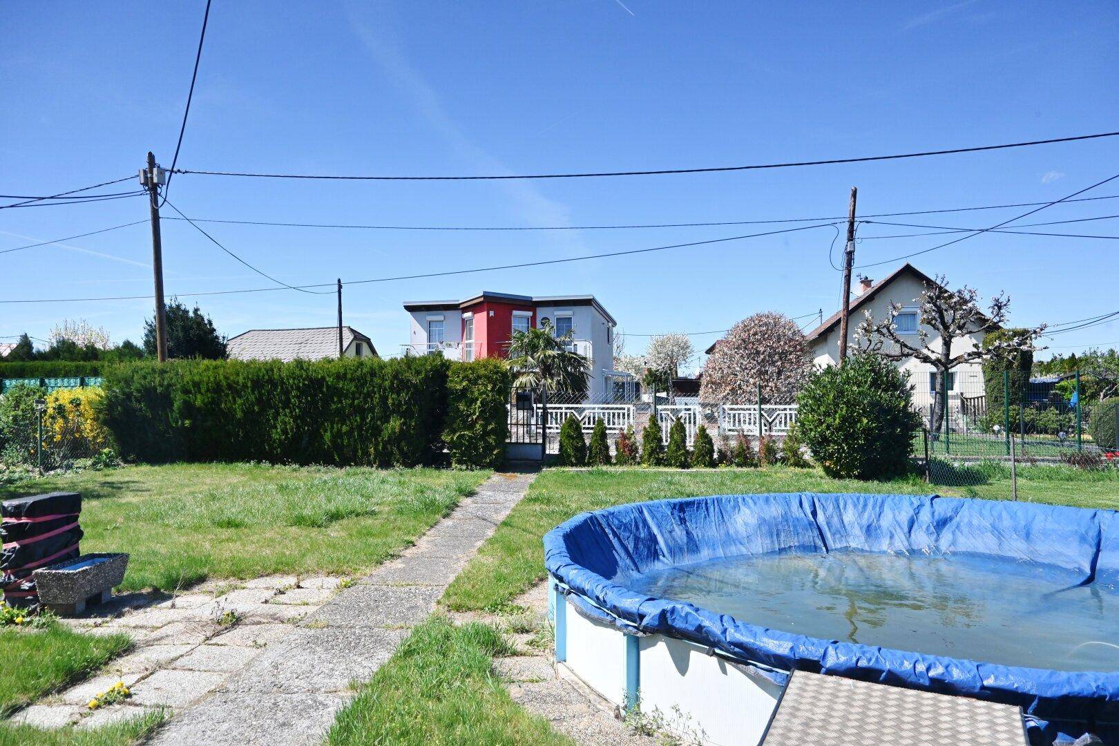 Gartenbereich mit Aufstellpool, Rasenfläche und einem gepflasterten Weg.