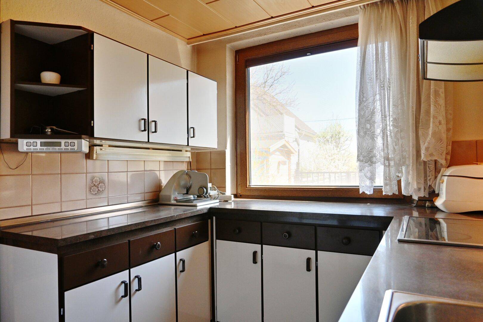 Helle Küche mit weißen und braunen Schränken, Fliesenrückwand und großem Fenster.