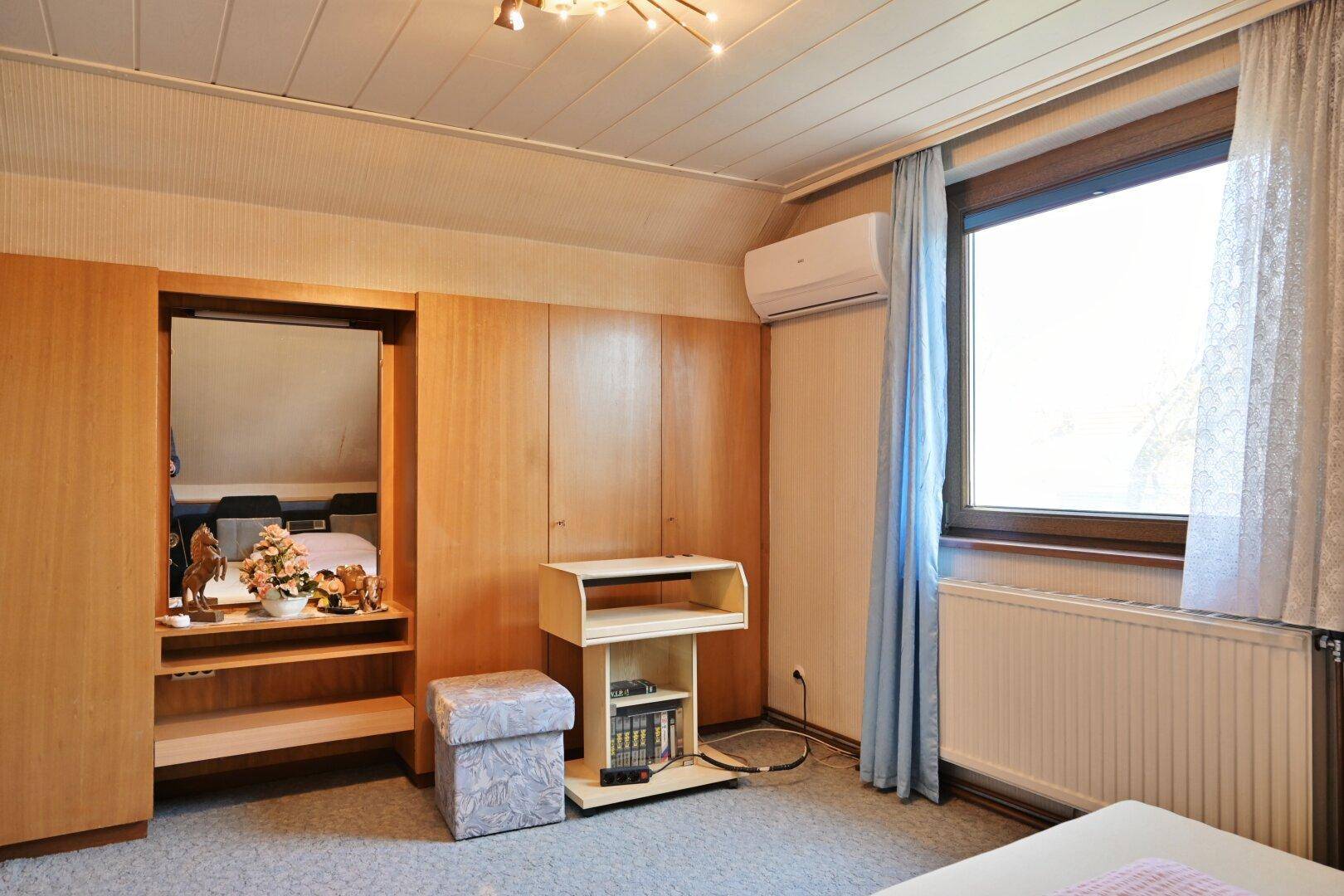 Schlafzimmer im Dachgeschoss mit Holzschränken, Klimaanlage und Fenster.