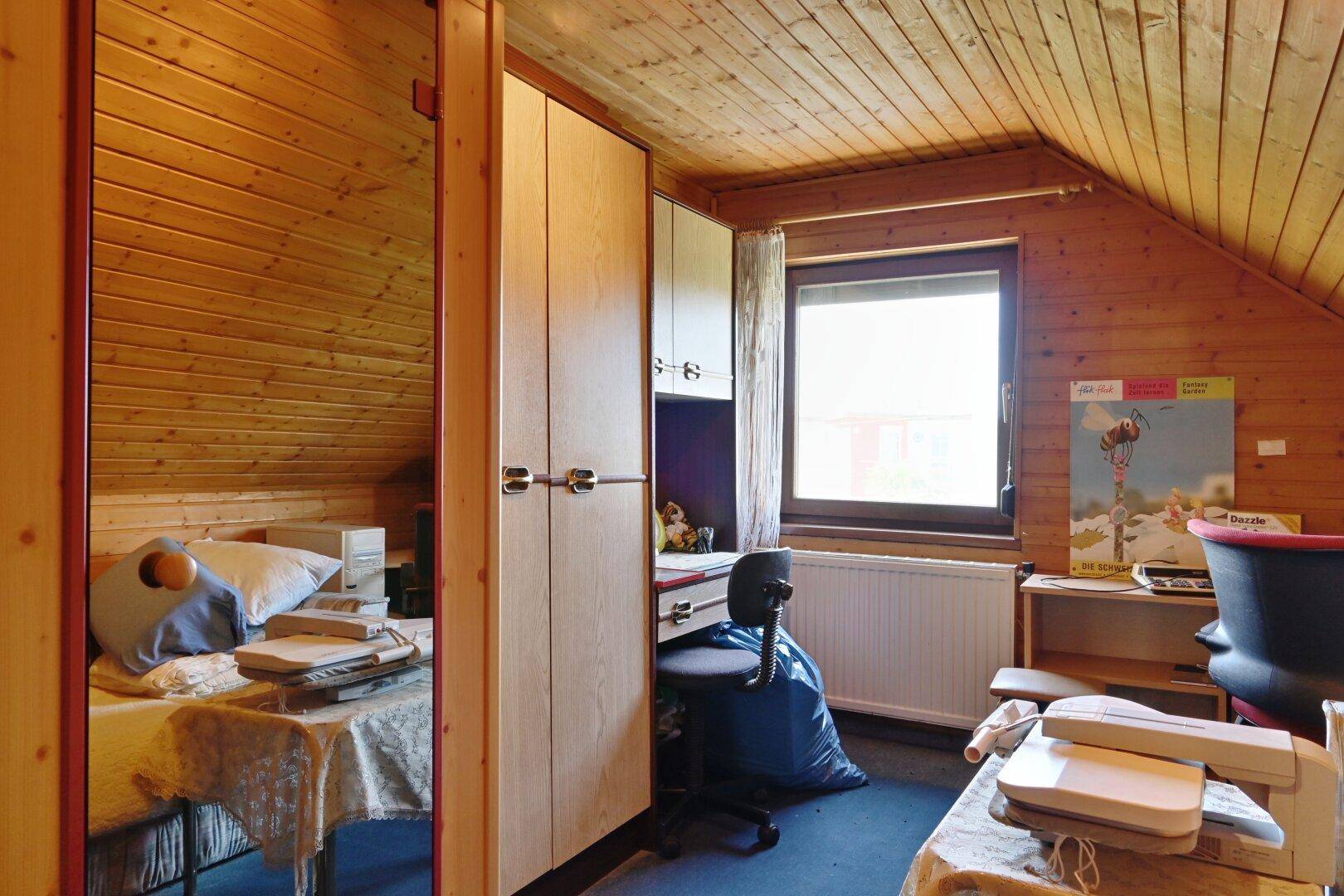 Kinderzimmer im Dachgeschoss mit Holzvertäfelung, Schreibtisch und Fenster.