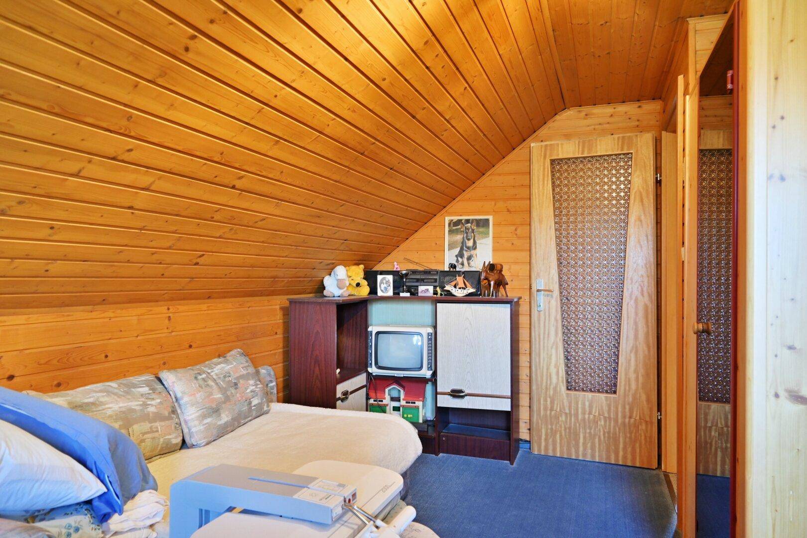 Gemütlicher Raum im Dachgeschoss mit Holzvertäfelung, Sofa und Teppichboden.