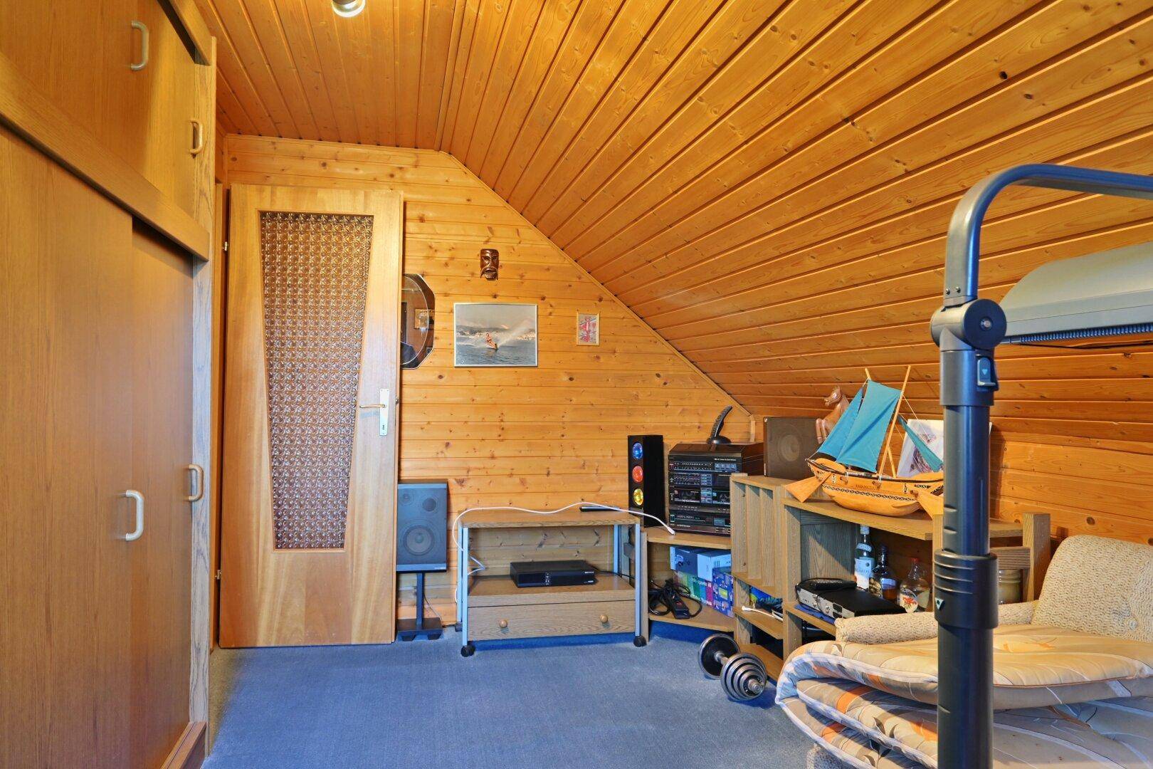 Dachgeschossraum mit Holzvertäfelung, Schränken und Teppichboden, vielseitig nutzbar.