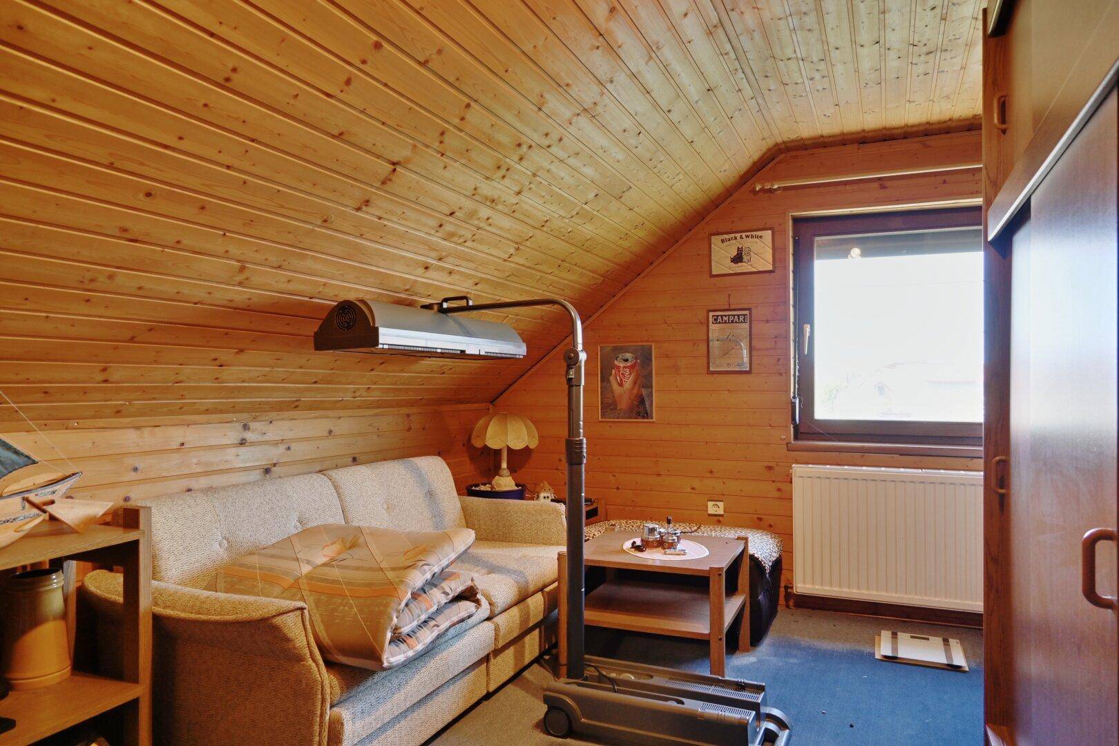Dachgeschosszimmer mit Holzvertäfelung, Sofa und Fenster, das Tageslicht spendet.