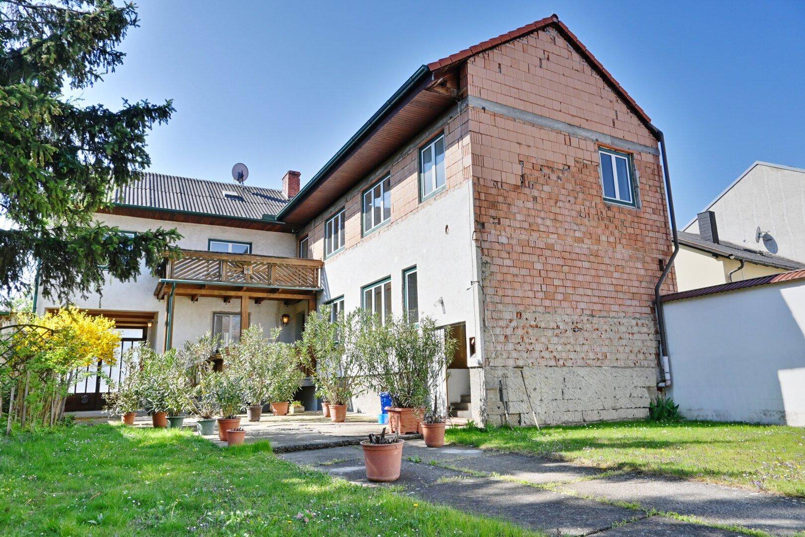 Rückansicht des Hauses mit Balkon, Gartenbereich und teilweise unverputzter Ziegelwand.