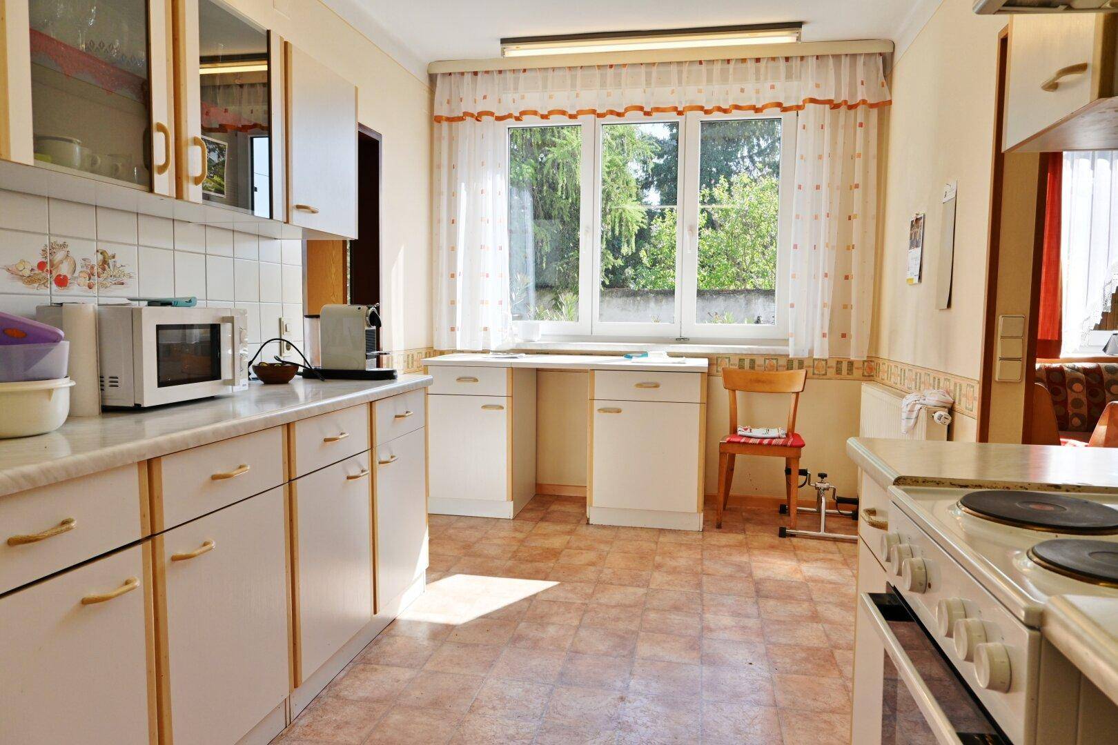 Helle Küche mit Fenster, weißen Schränken und Arbeitsbereich unter dem Fenster.