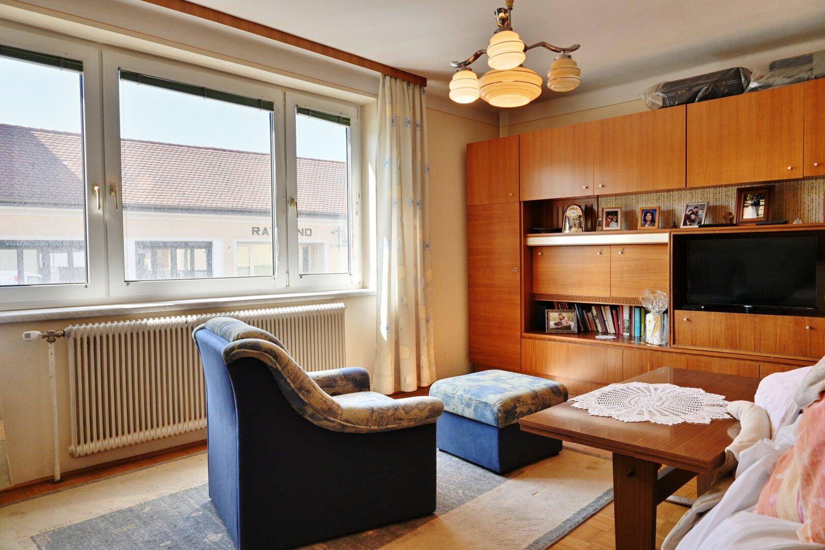 Gemütliches Wohnzimmer mit Holzmöbeln, blauem Sessel und Blick auf die Straße.
