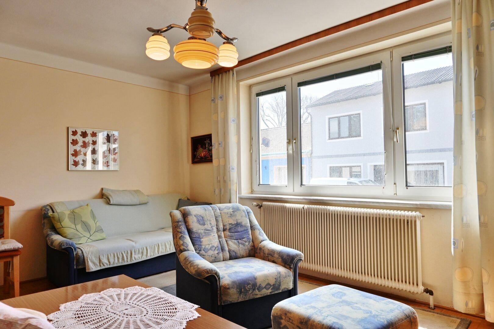 Helles Wohnzimmer mit großem Fenster, beigem Sofa und traditioneller Einrichtung.