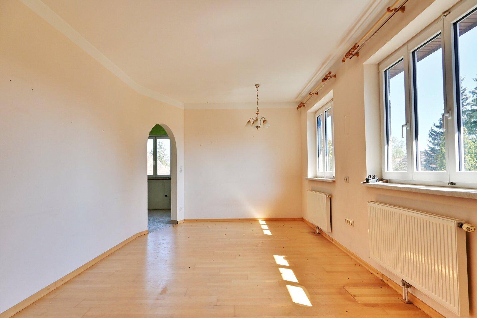 Geräumiger, leerer Raum mit Parkettboden, hohen Decken und großen Fenstern.
