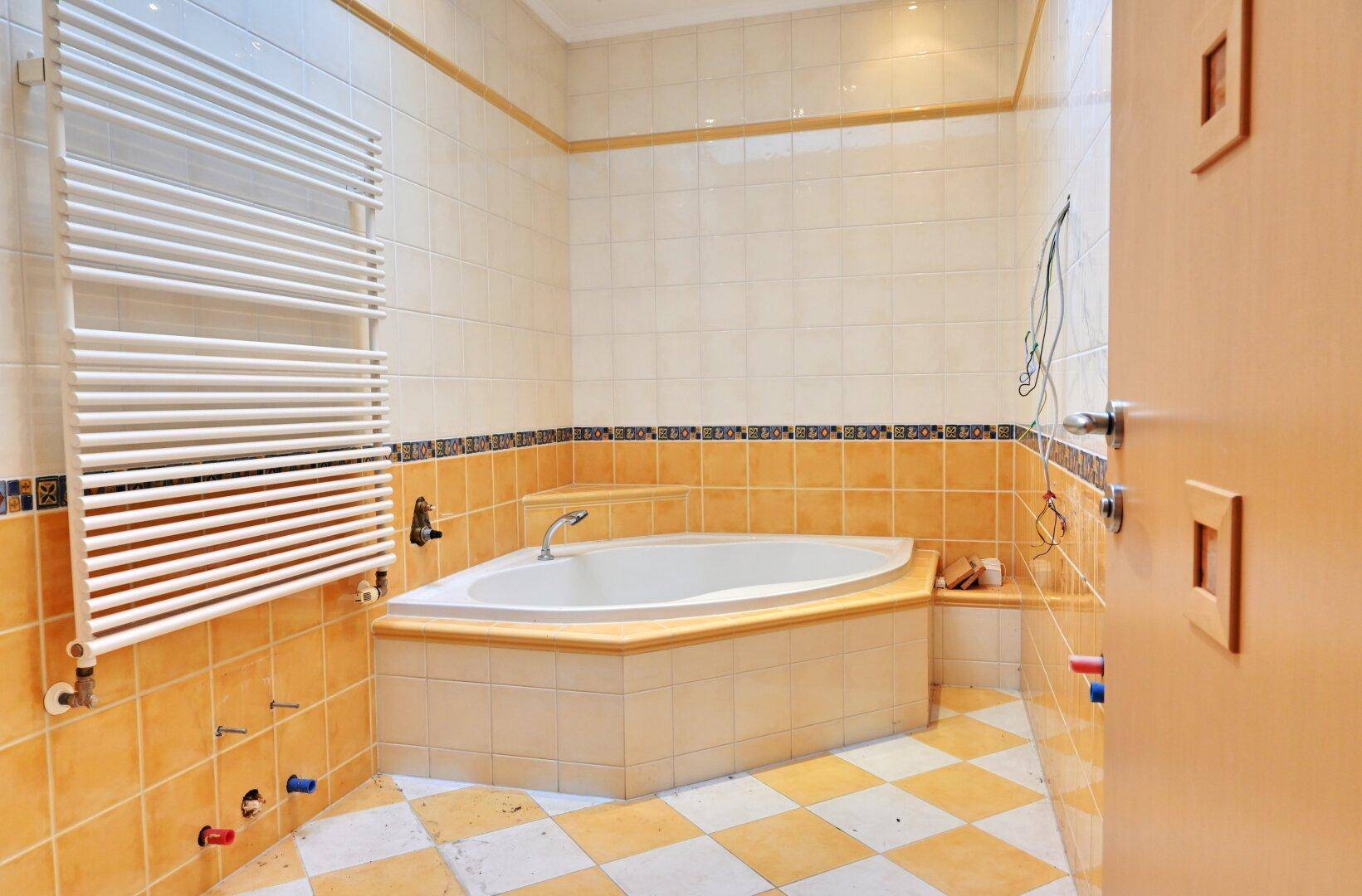 Badezimmer mit Eckbadewanne, gelben und weißen Fliesen sowie Handtuchheizkörper.