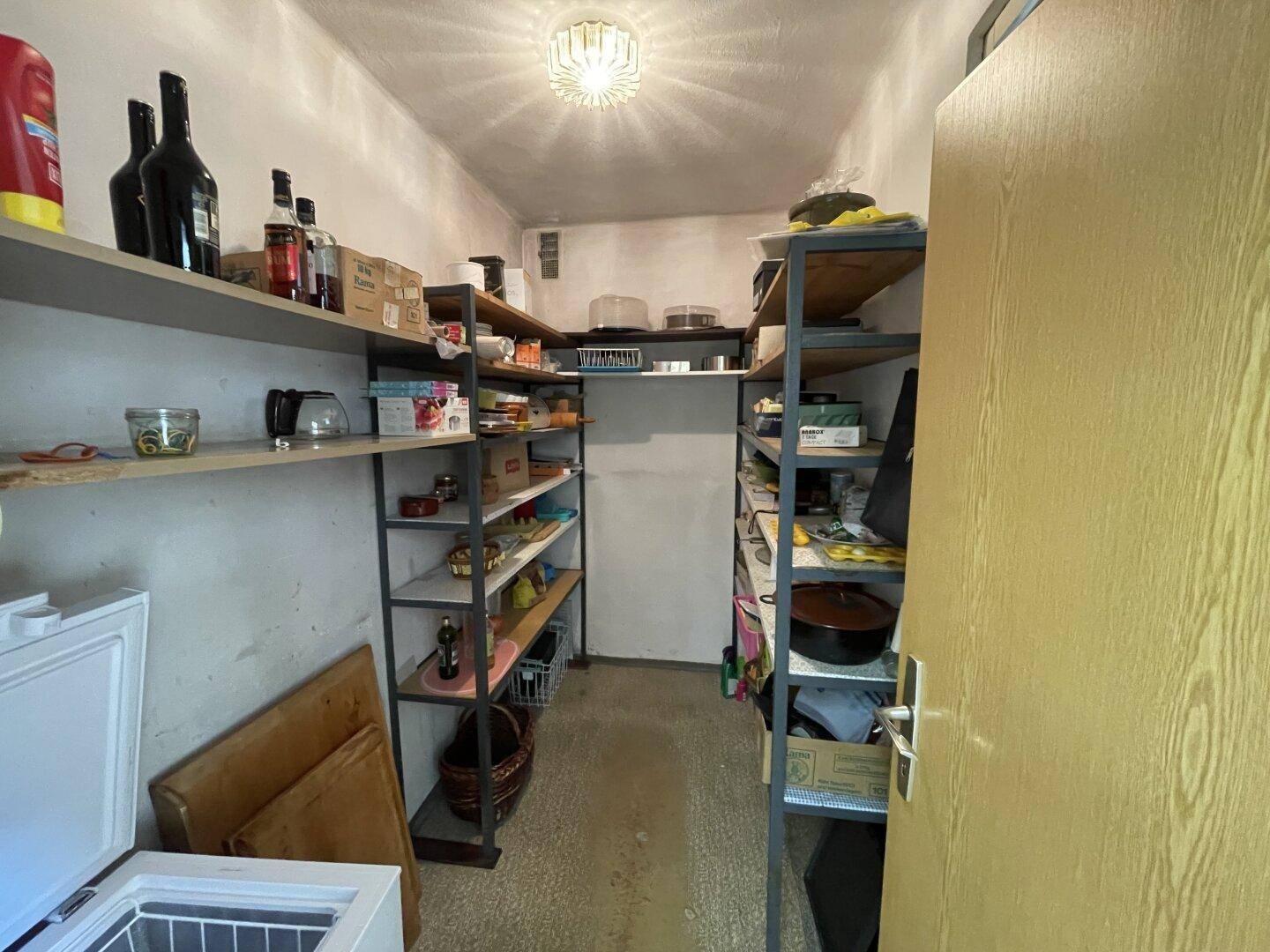Vorratsraum mit Regalen, gefüllt mit Lebensmitteln und Getränken, sowie einem Gefrierschrank.