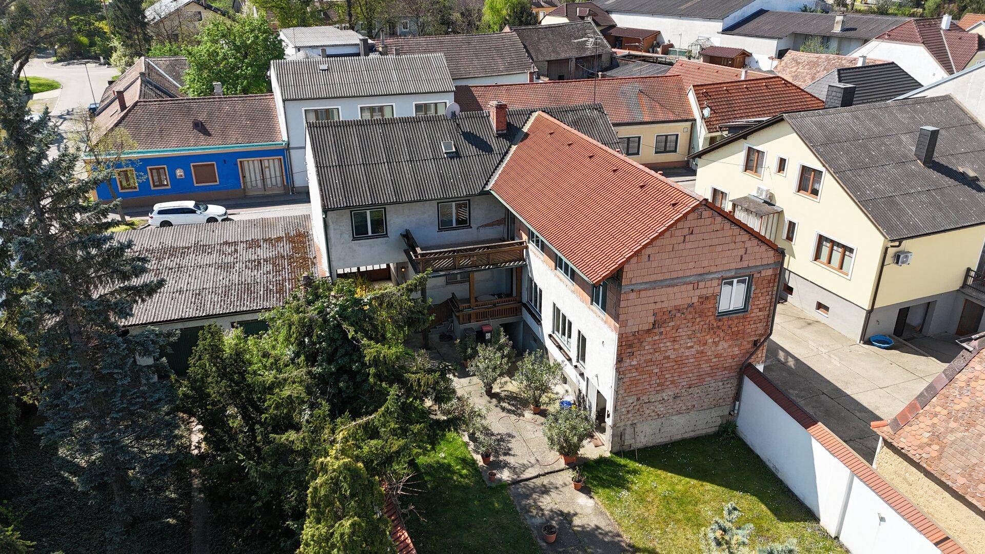 Luftaufnahme eines Wohngebiets mit verschiedenen Häusern und Gärten unter blauem Himmel.