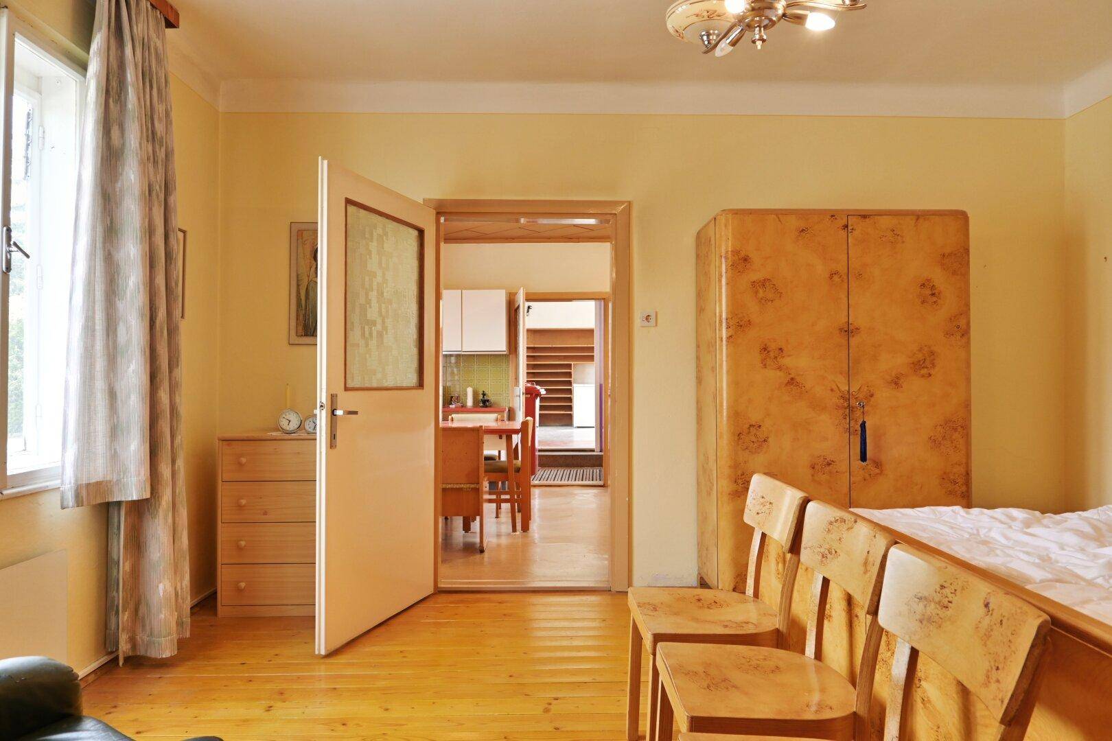 Schlafzimmer mit Holzboden und Blick durch eine offene Tür in einen angrenzenden Raum.