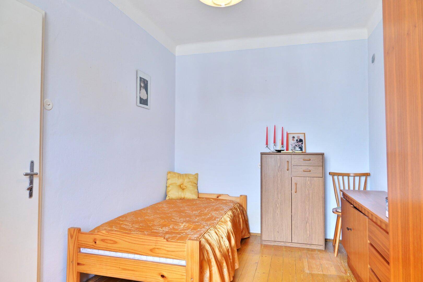 Kleines Schlafzimmer mit hellem Holzboden, einem Einzelbett und blauen Wänden.