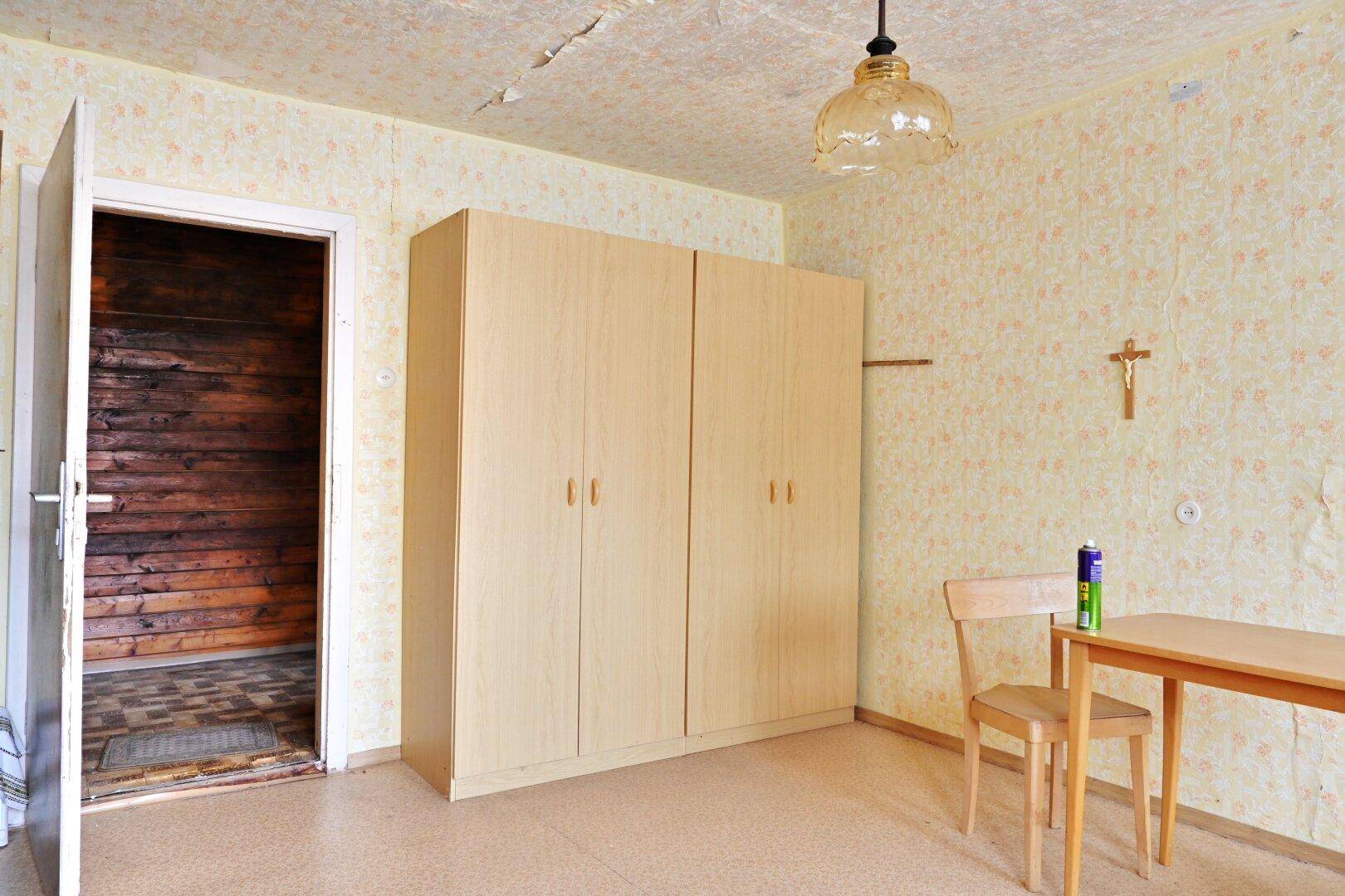 Raum mit gemusterter Tapete, einem Kleiderschrank und einem Holztisch, der Renovierung benötigt.