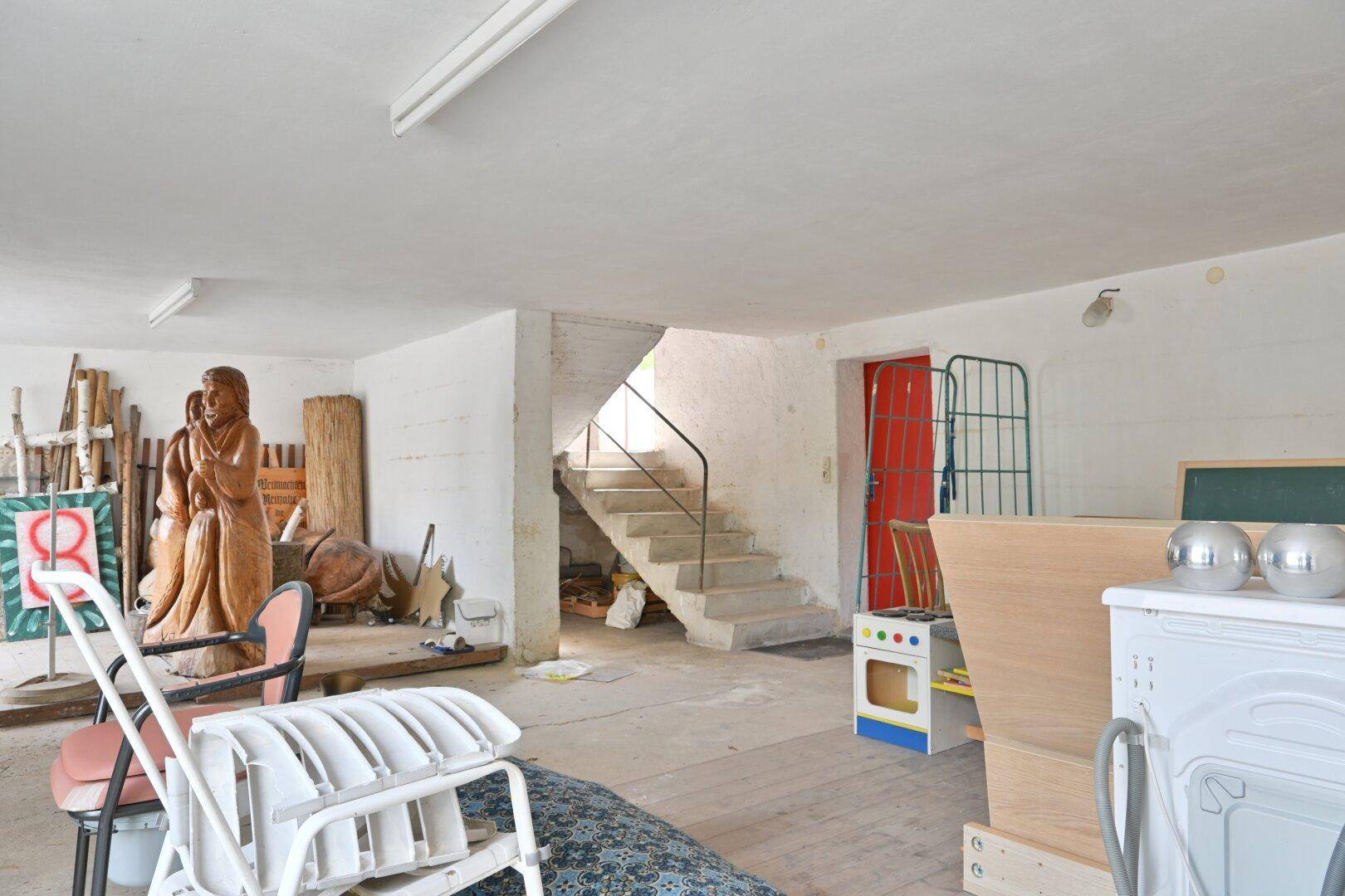 Kellerraum mit Betonboden, einer Treppe und verschiedenen Gegenständen, die gelagert werden.