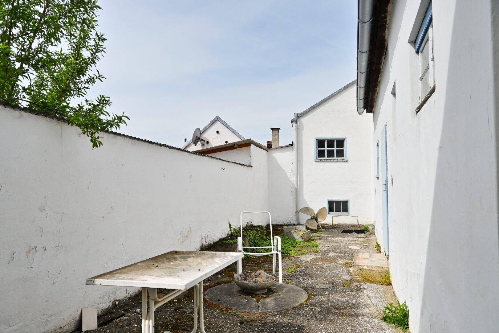 Kleiner, ummauerter Hinterhof mit einem Tisch und Stühlen, ideal für eine Sitzecke im Freien.