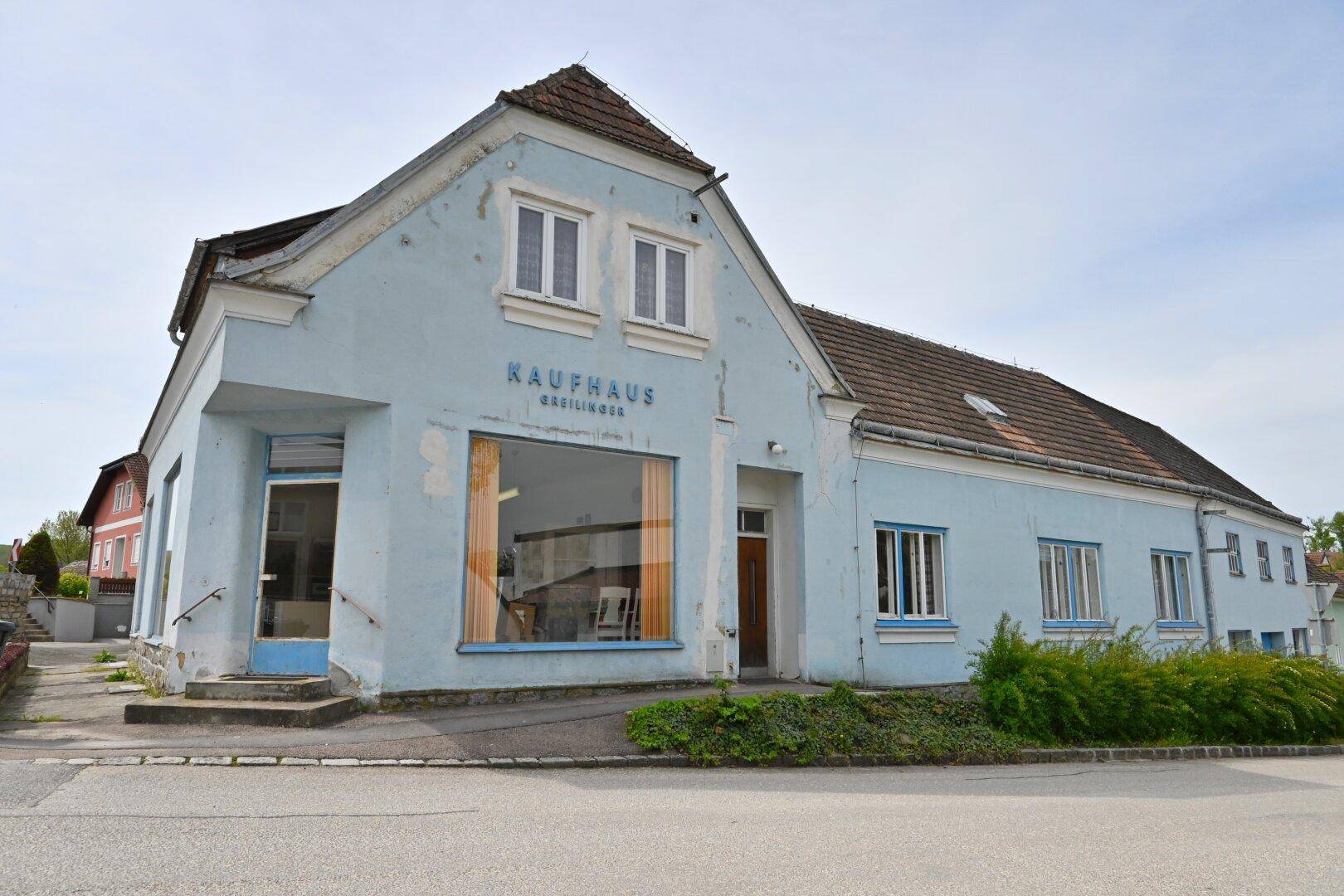 Ansicht der hellblauen Fassade des Gebäudes mit großen Schaufenstern und einem Eingangsbereich.