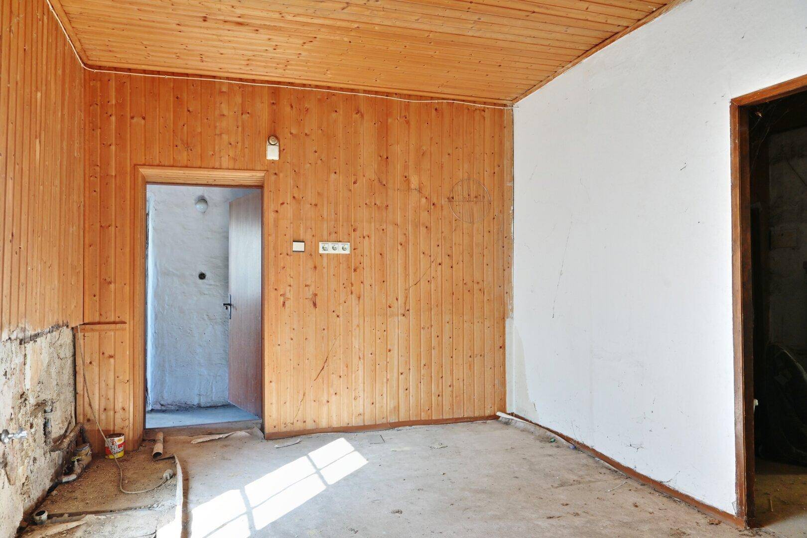 Innenraum mit Holzvertäfelung an Decke und einer Wand, der auf eine Renovierung wartet.