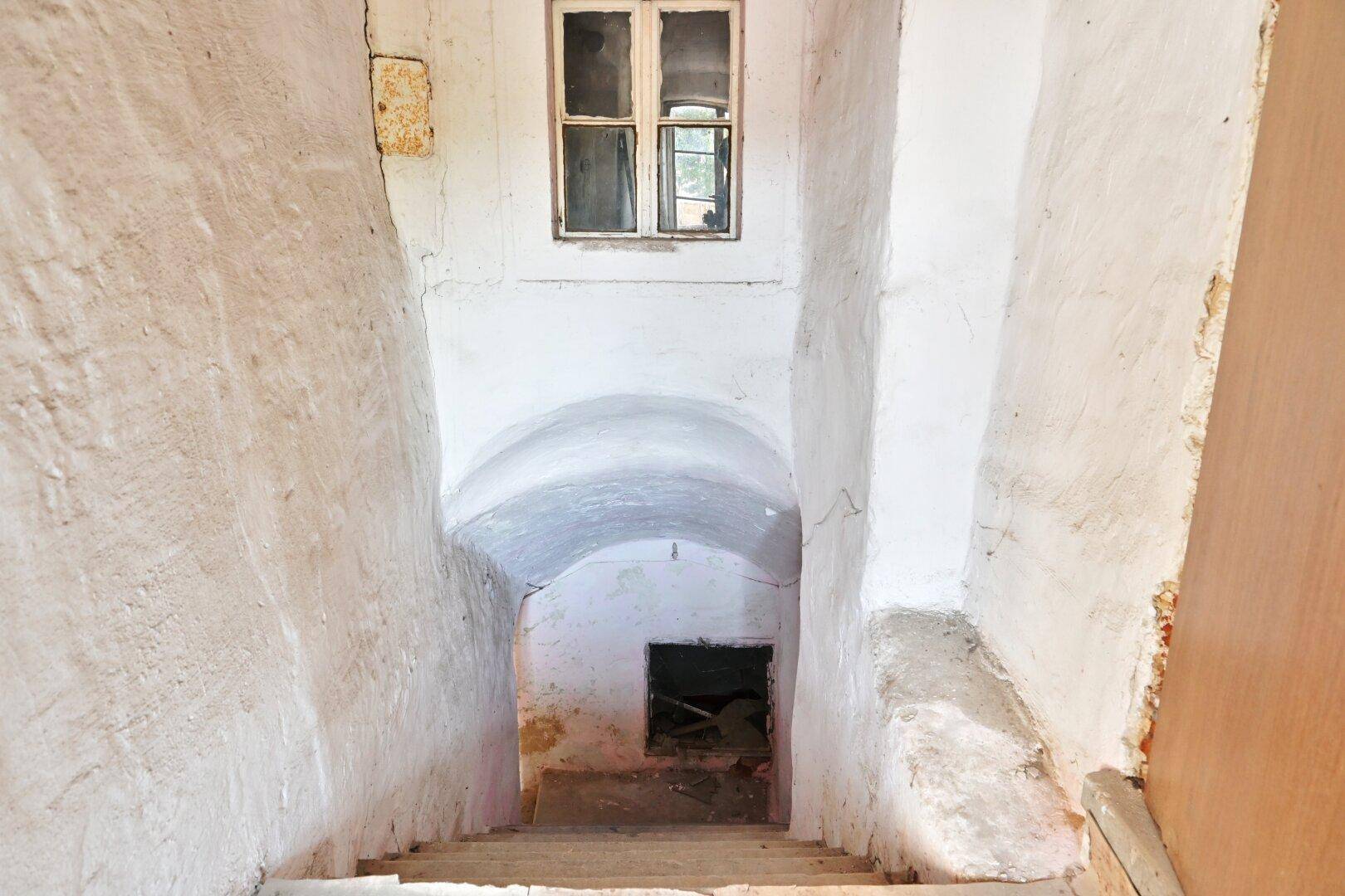 Treppe führt hinunter in einen gewölbten Kellerraum mit rauen, unverputzten Wänden.