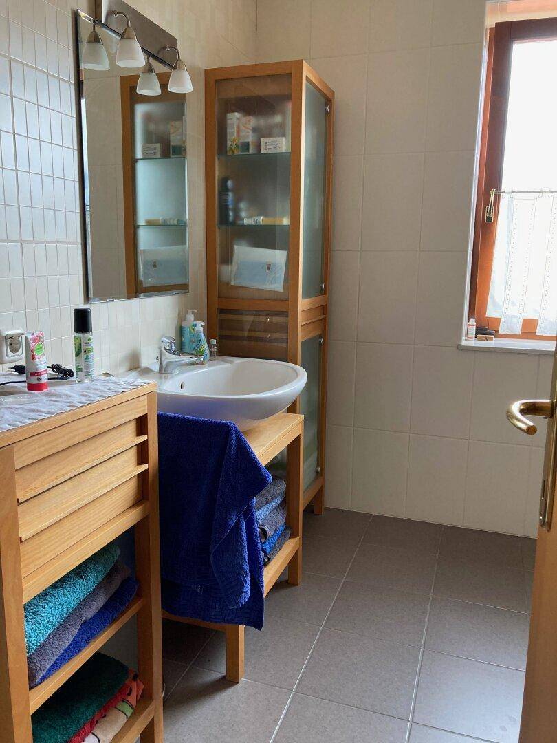 Badezimmer mit Einzelwaschbecken, Holzschränken und hellen Fliesen.