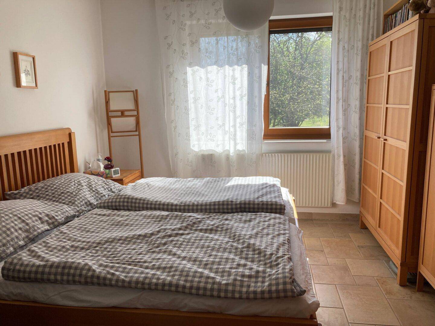 Helles Schlafzimmer mit Doppelbett, Holzschrank und Blick ins Grüne.