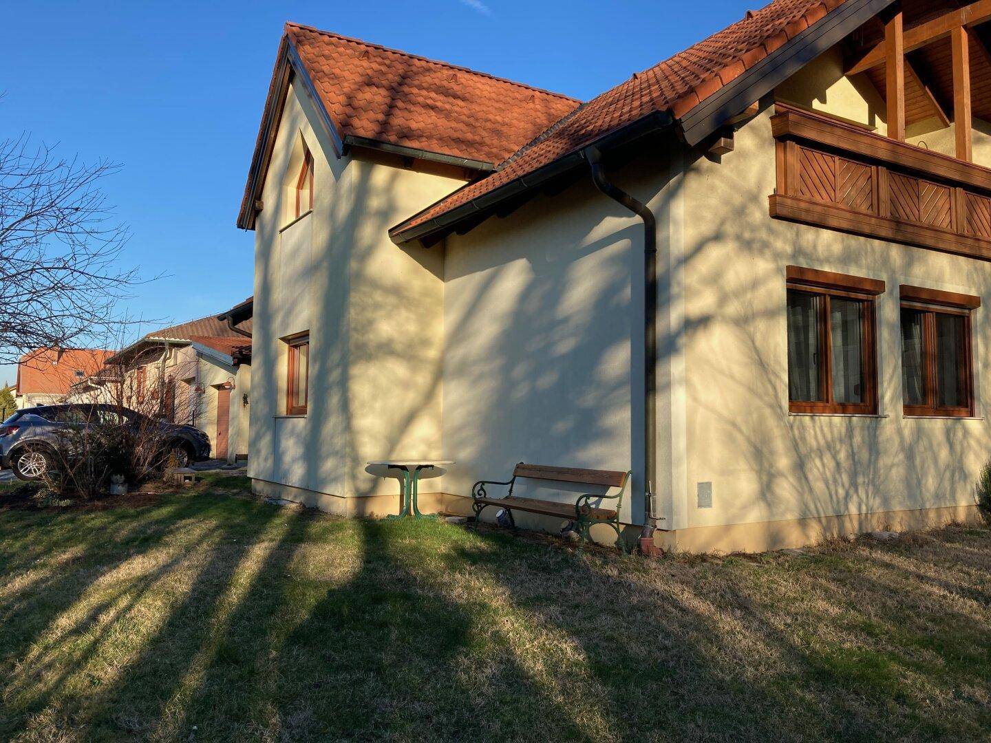 Hausfassade im warmen Abendlicht mit Gartenbank und gepflegtem Rasen.