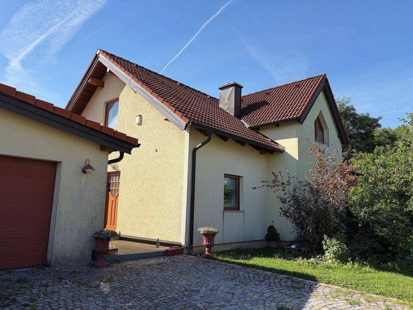 Rückansicht des Hauses mit Garage, gepflasterter Zufahrt und Gartenbereich.