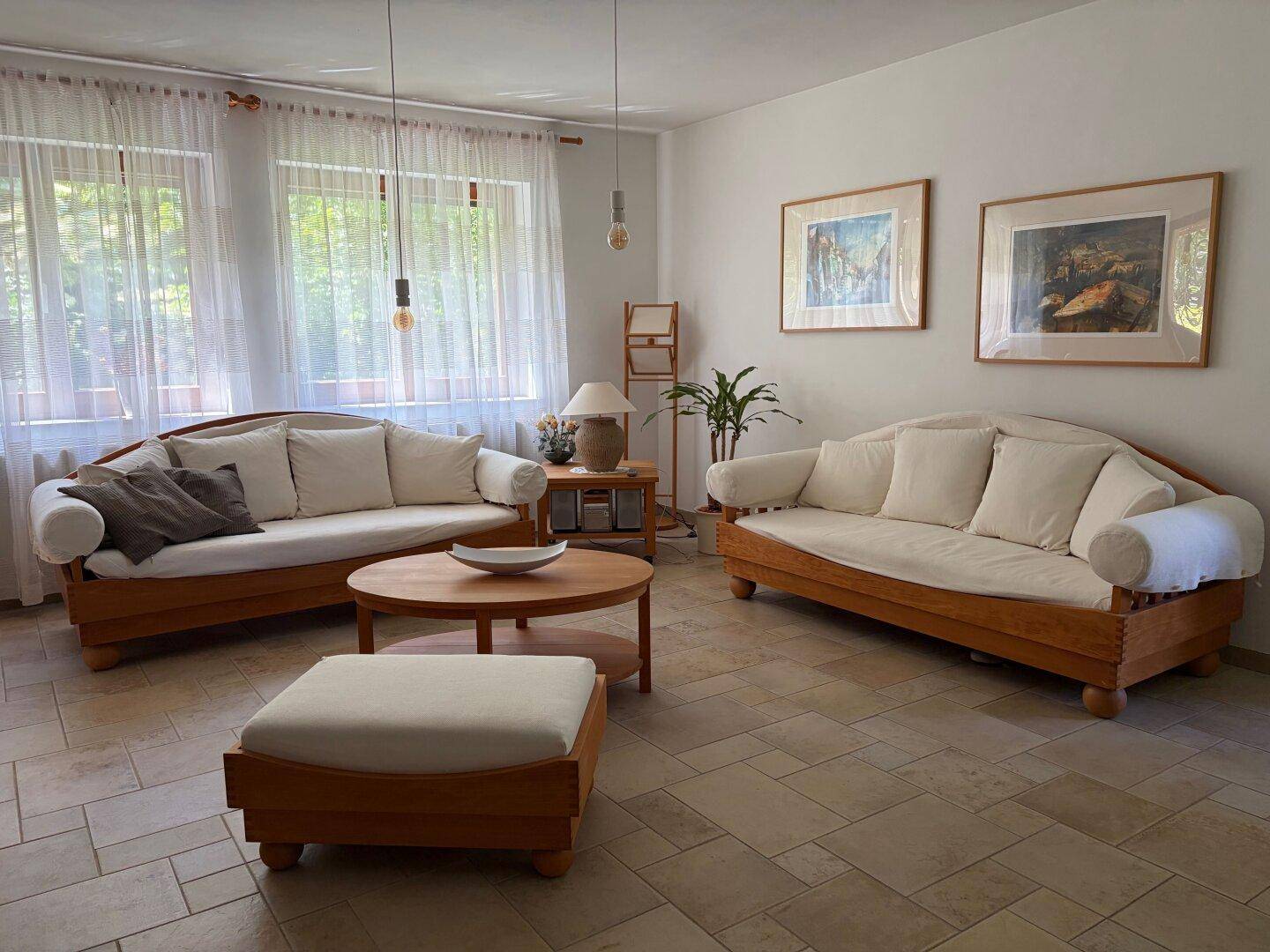 Gemütliches Wohnzimmer mit zwei hellen Sofas, Holztisch und großen Fenstern.