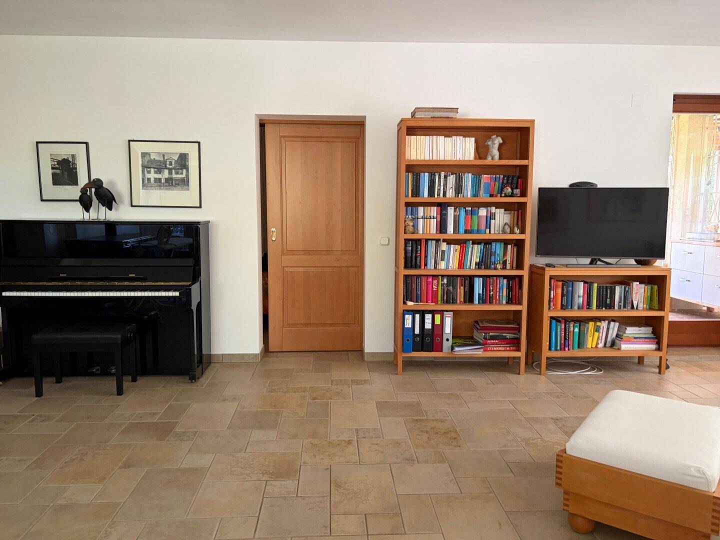 Geräumiger Wohnbereich mit Klavier, Bücherregalen und hellem Fliesenboden.