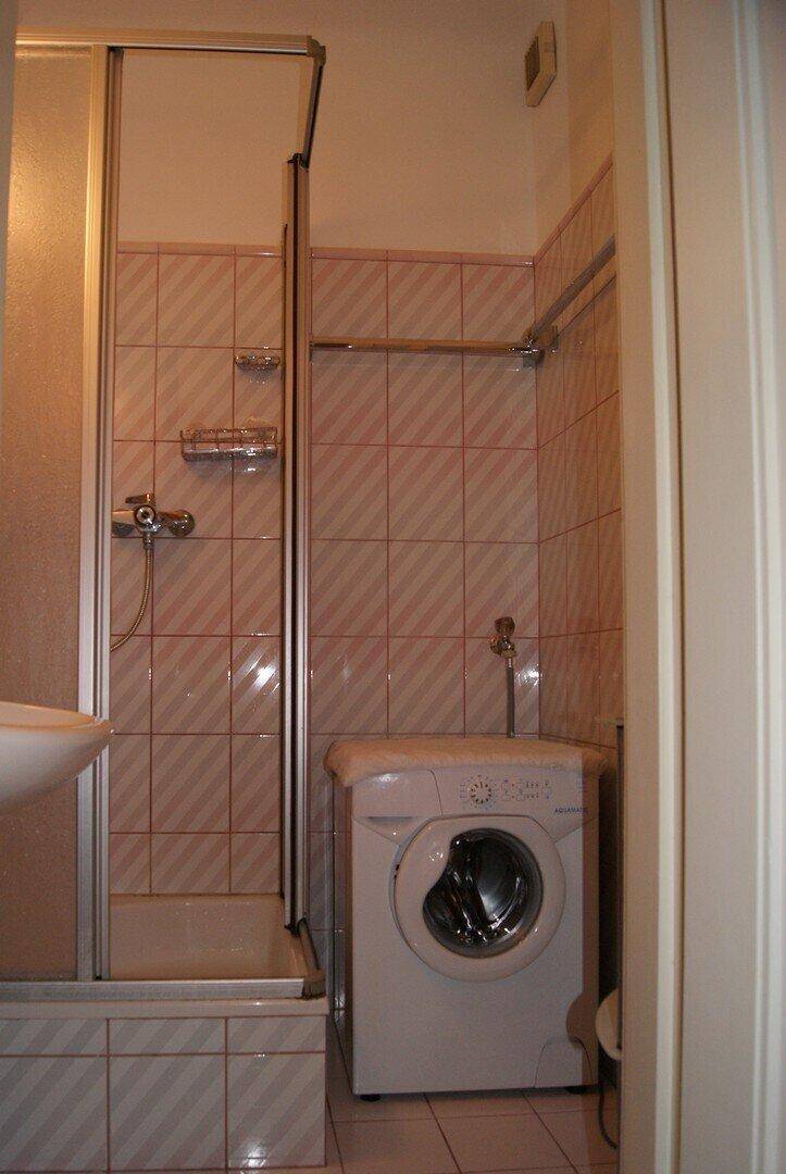 Kleines Badezimmer mit rosa-weißen Fliesen, Duschkabine und integrierter Waschmaschine.