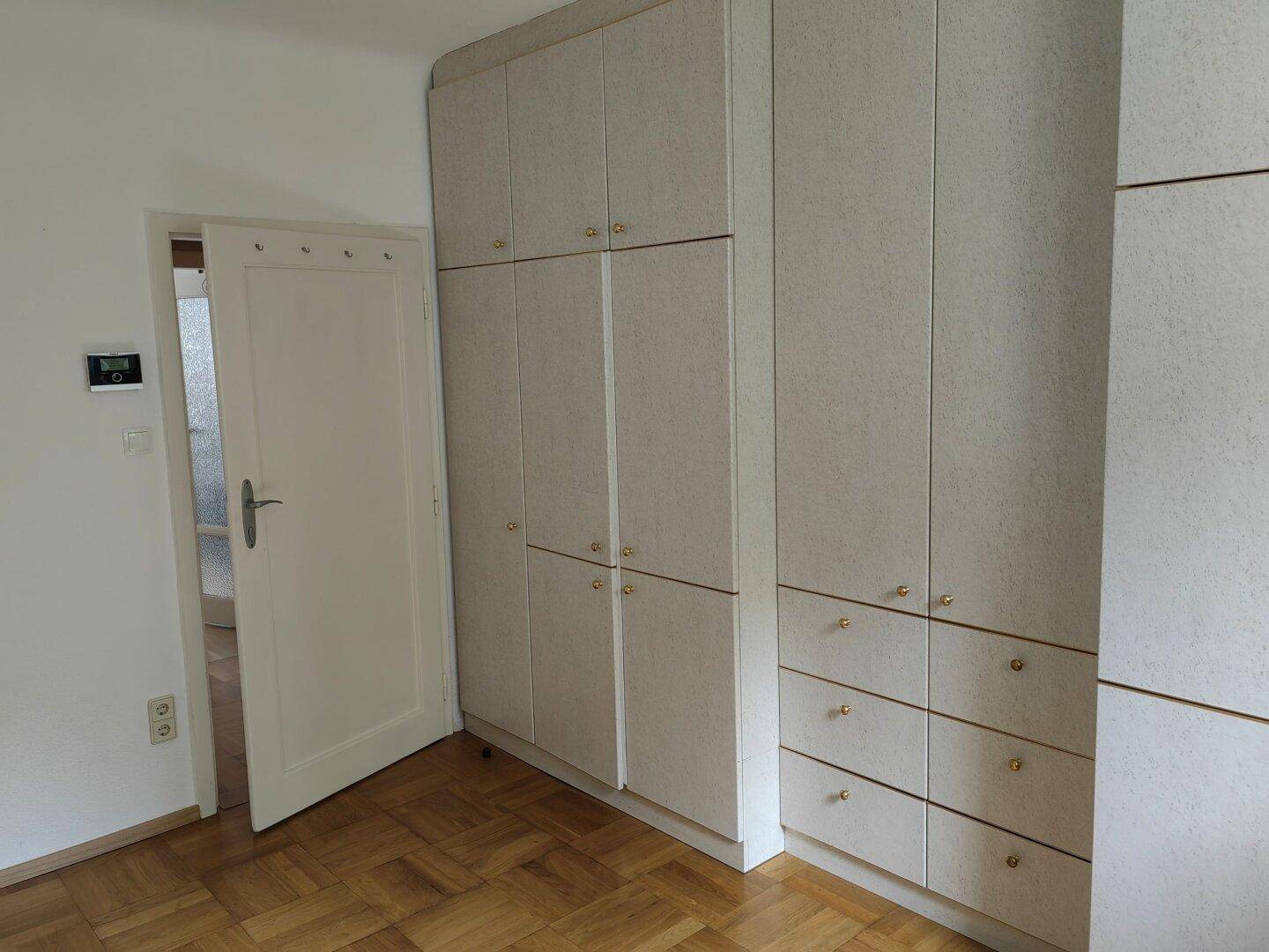 Geräumiges Schlafzimmer mit umfangreichen hellen Einbauschränken und Zugang zu einem weiteren Raum.