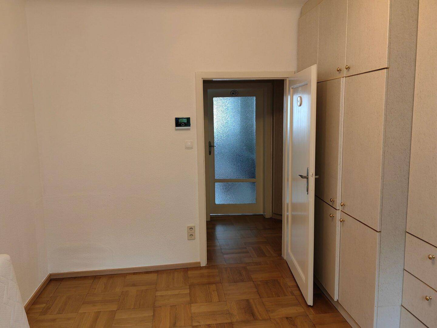 Schlafzimmer mit Einbauschränken und einer Tür, die zu einem Flur mit Milchglastür führt.