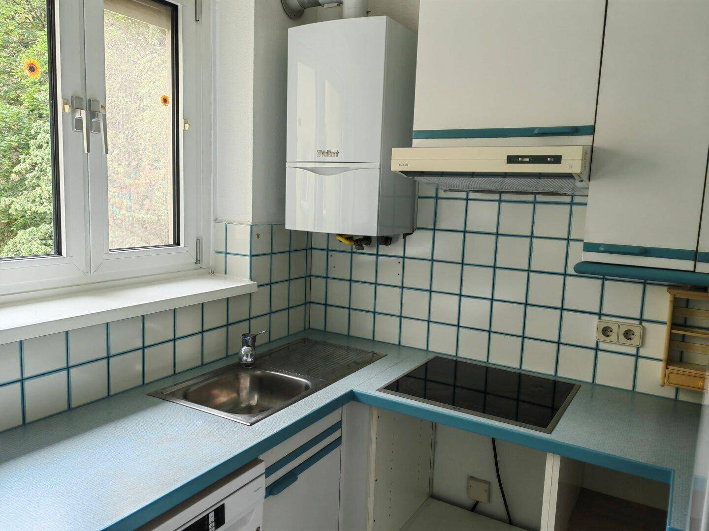 Küche mit blauen Fliesen, Spüle und Fenster mit Blick ins Grüne.