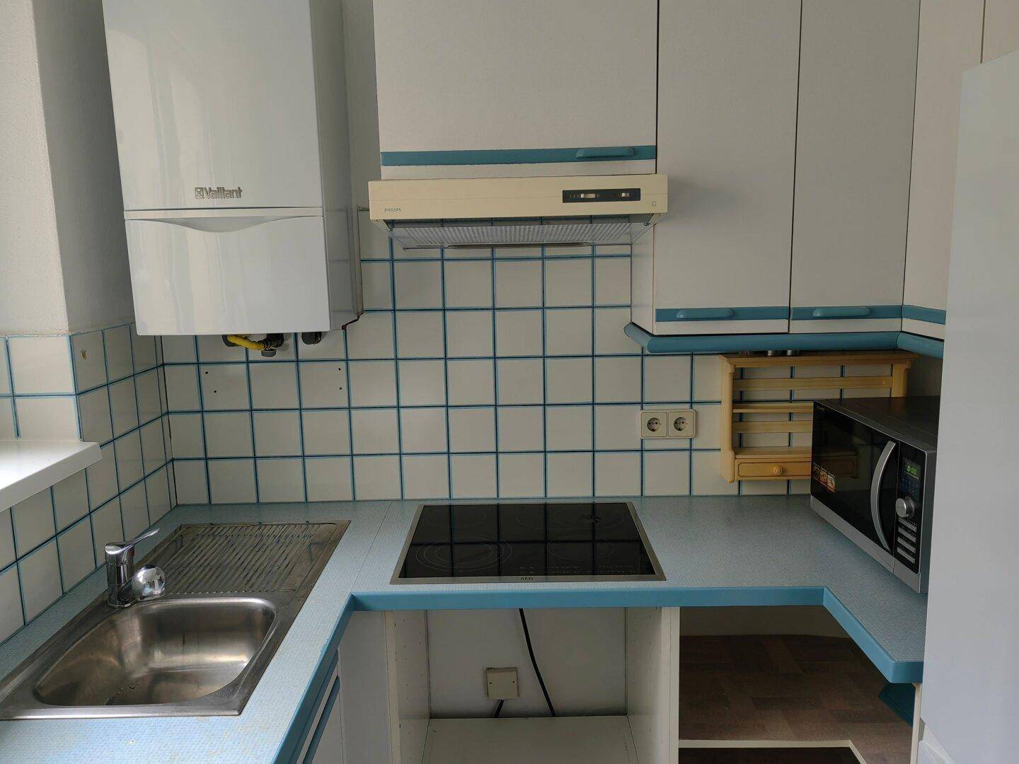 Küche mit blauen und weißen Fliesen, Spüle, Induktionskochfeld und Wandheizkessel.