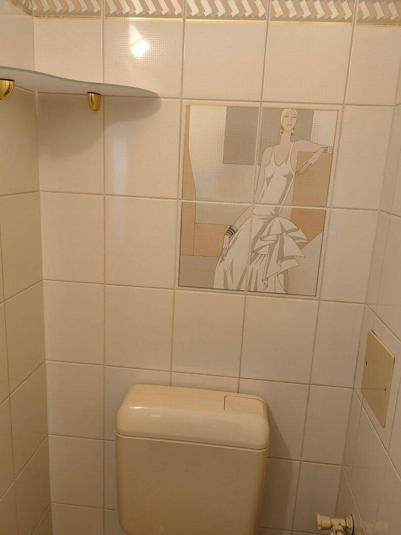 WC mit beigen Fliesen, Toilette und dekorativem Fliesenbild.