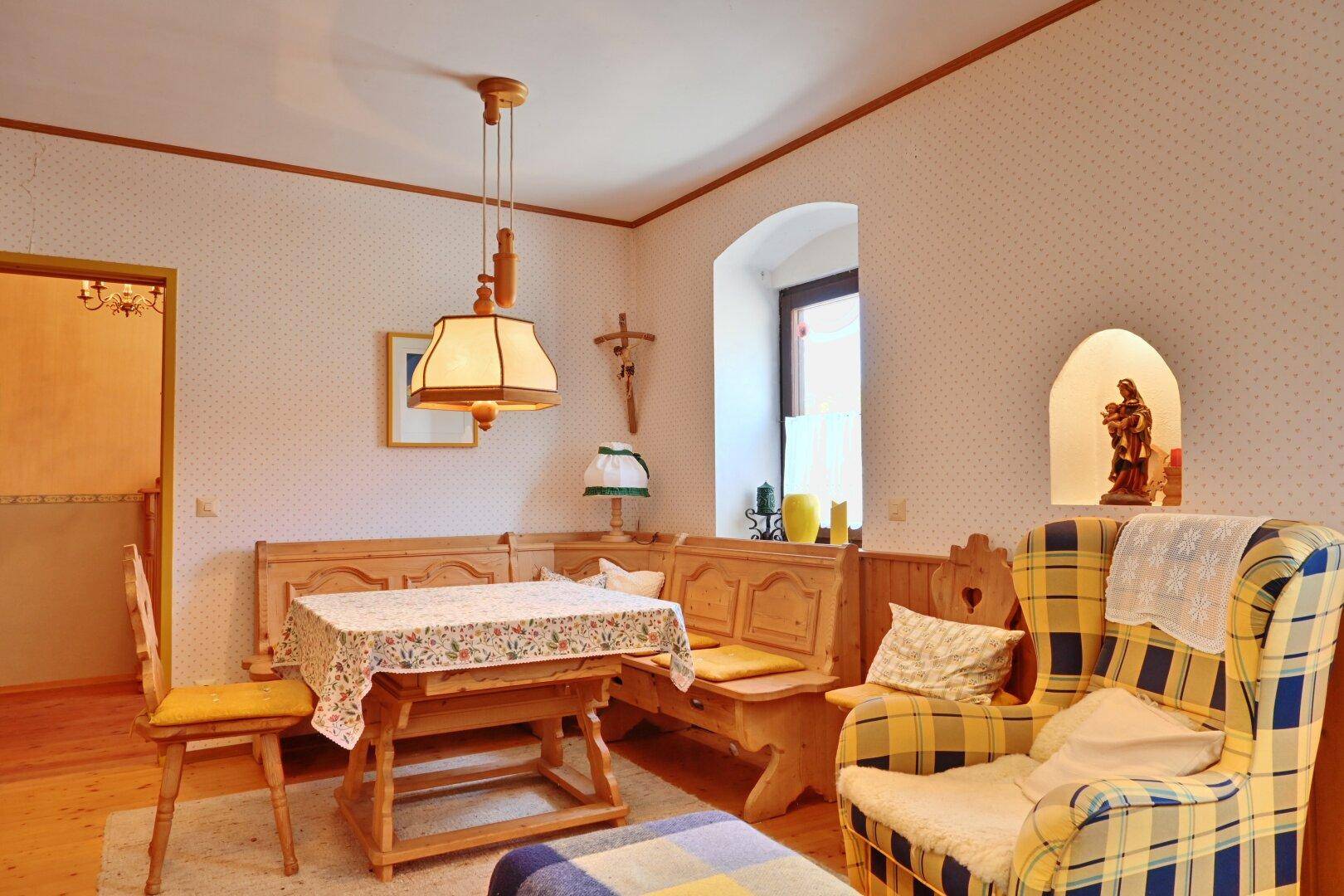 Gemütlicher Essbereich mit traditioneller Eckbank, Holztisch und kariertem Sessel in ländlichem Stil.