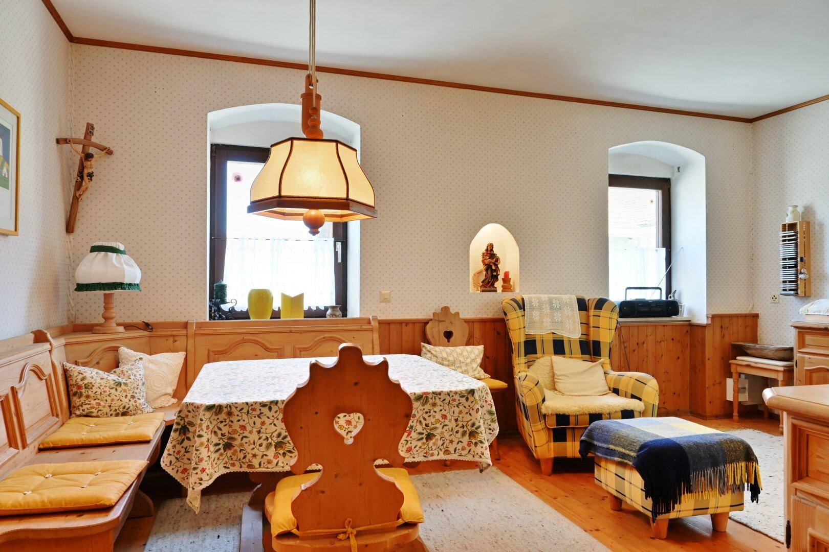 Rustikaler Wohn- und Essbereich mit traditionellen Holzmöbeln, Eckbank und kariertem Sessel.