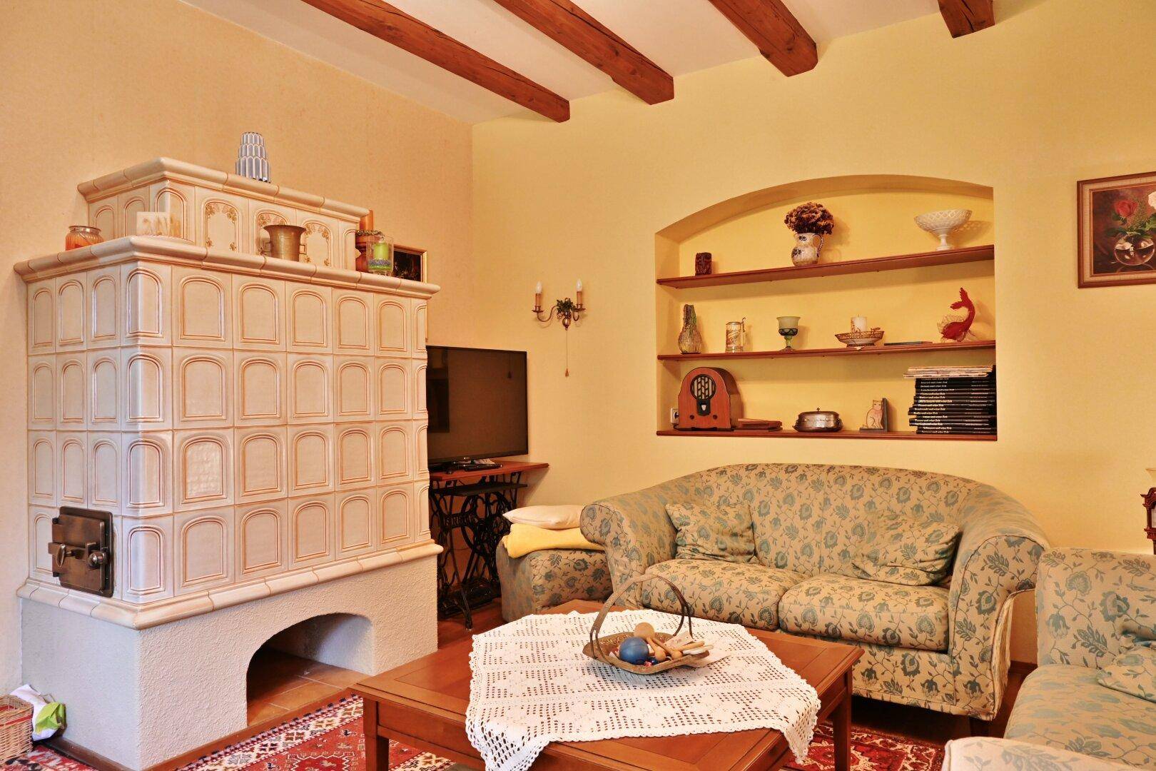 Gemütliches Wohnzimmer mit Kachelofen, freiliegenden Holzbalken und traditionellen Sofas.