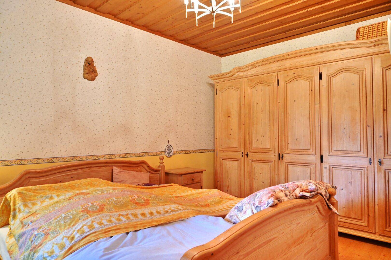 Gemütliches Schlafzimmer im Landhausstil mit Holzmöbeln, Holzbalkendecke und traditioneller Tapete.