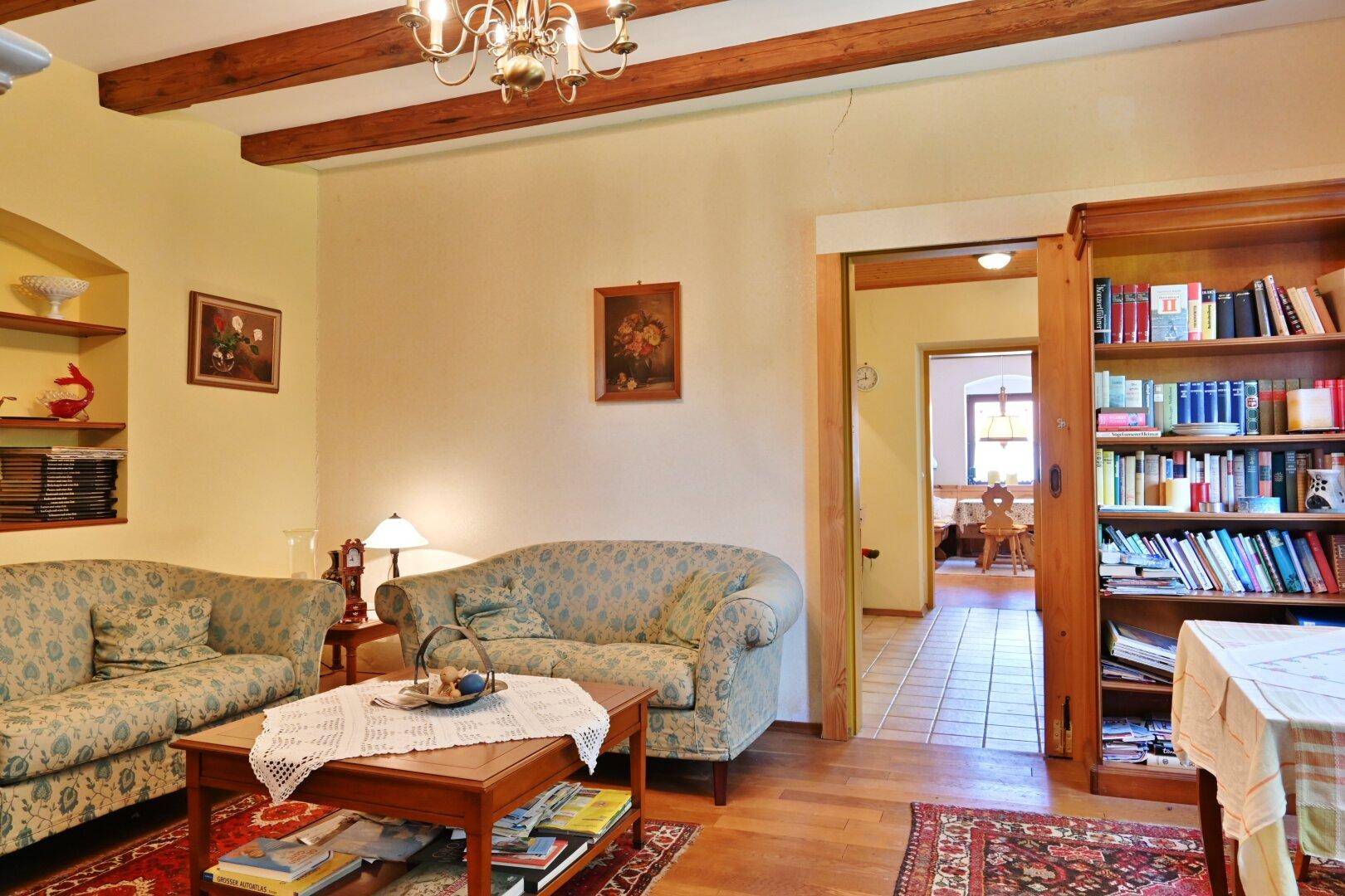 Geräumiges Wohnzimmer mit Holzbalkendecke, traditionellen Sofas und Durchgang zu weiteren Räumen.