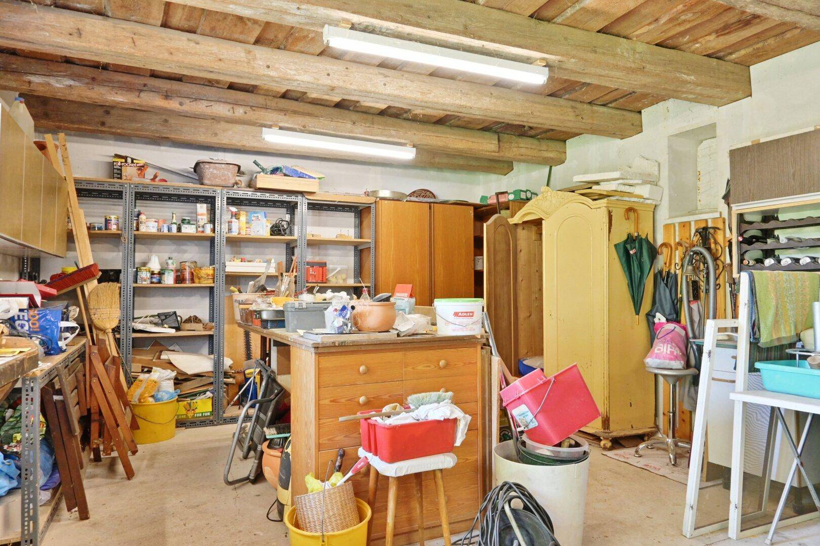 Geräumiger Werkstatt- oder Abstellraum mit Holzbalkendecke und vielen Regalen für Lagerung.