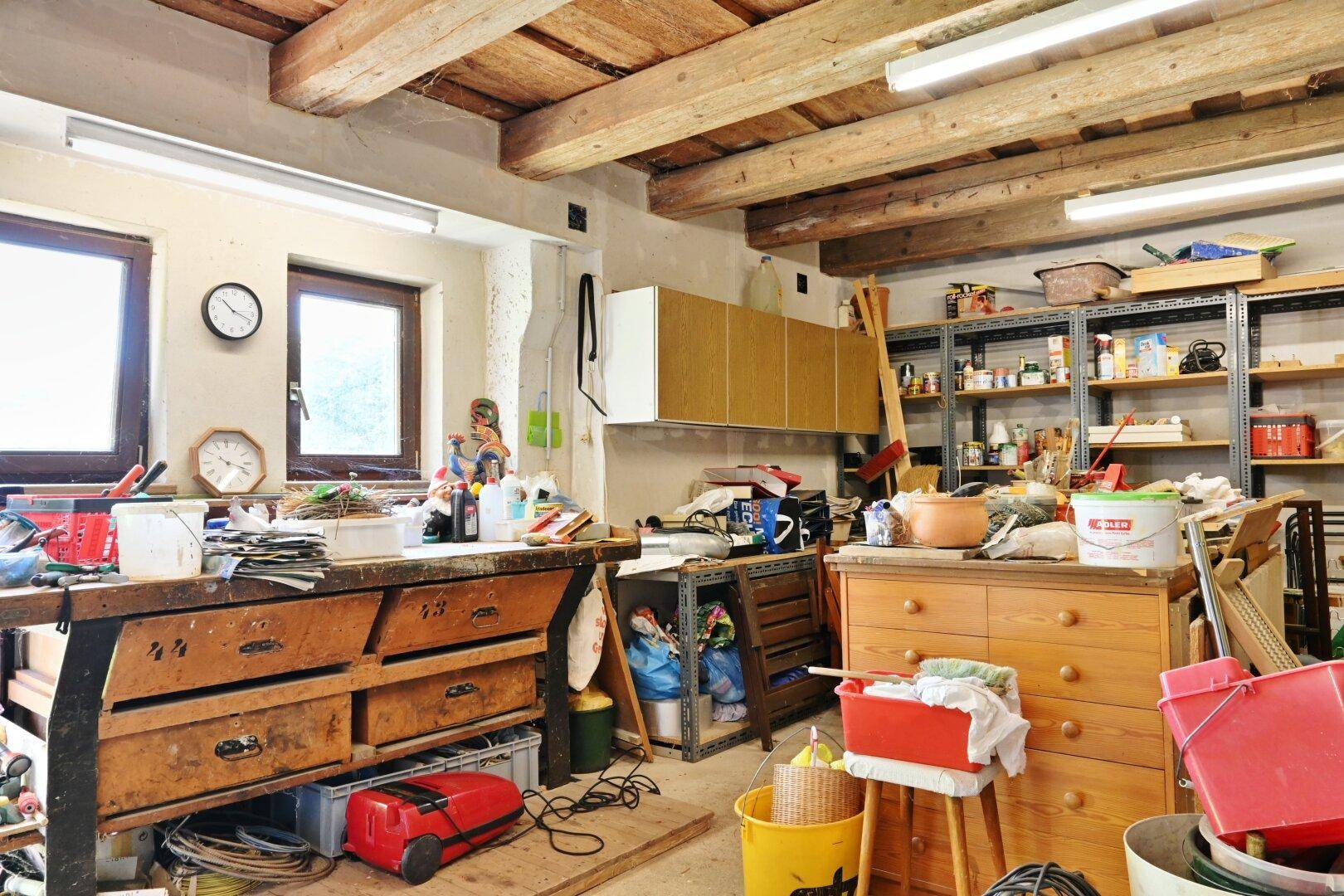Heller Werkstattraum mit Fenstern, Holzbalkendecke und umfangreichen Arbeits- und Lagerflächen.