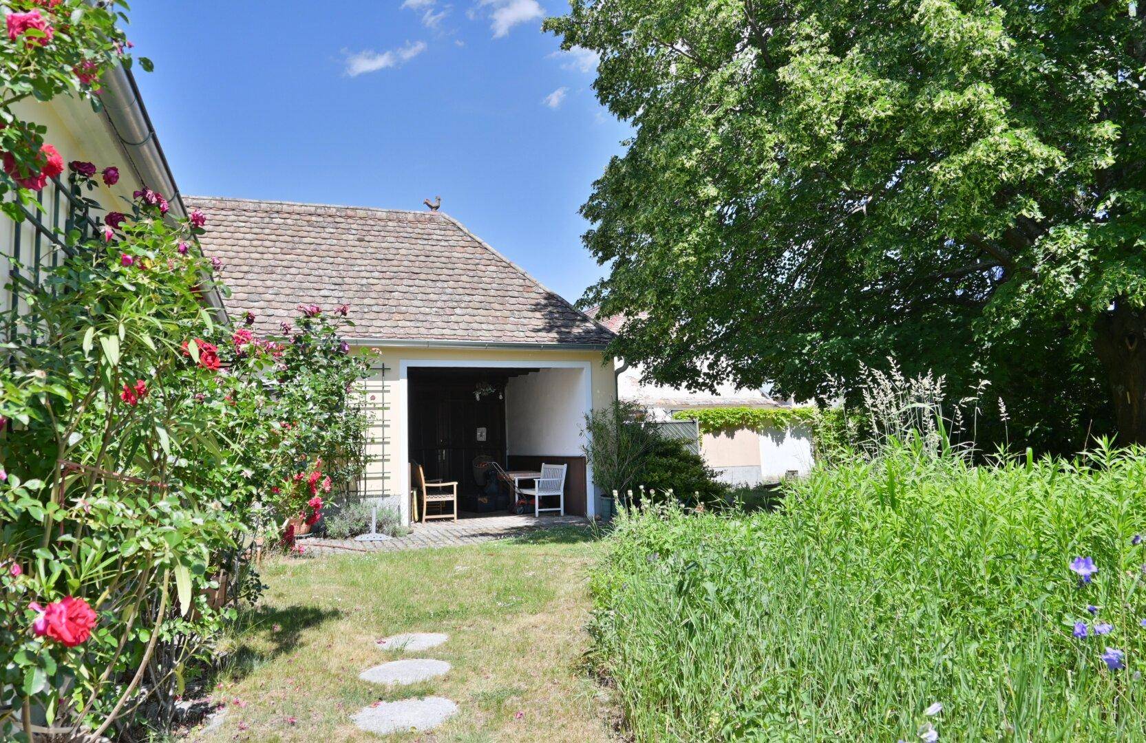 Gartenweg führt zu einem überdachten Außenbereich mit Sitzgelegenheiten und viel Grün.