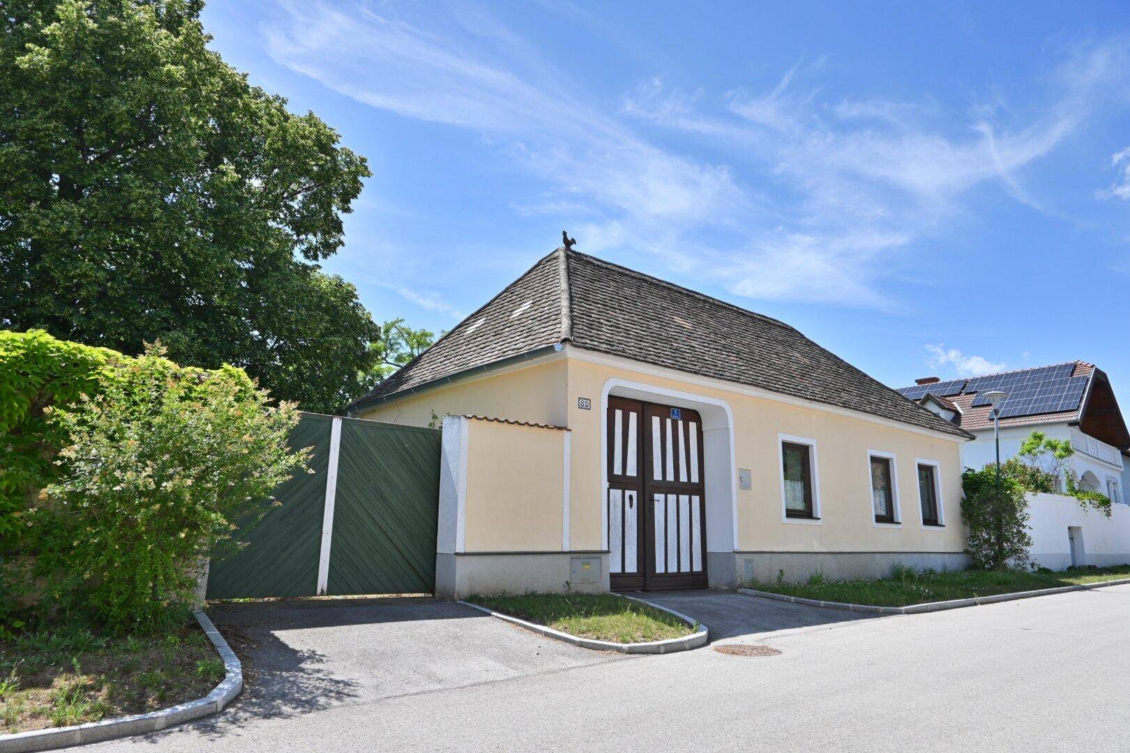 Traditionelles Landhaus mit gelber Fassade, Holztor und Satteldach an einer ruhigen Straße.