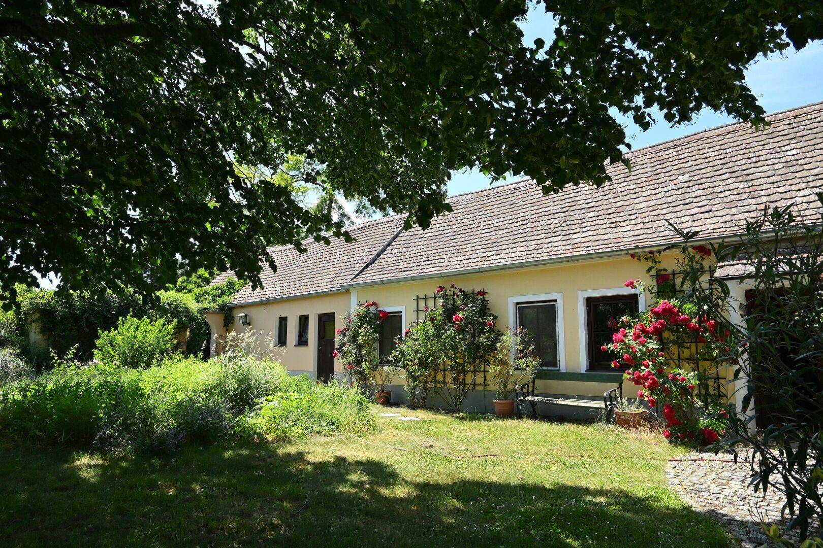 Charmantes Haus mit üppigem Garten, blühenden Rosen und schattenspendenden Bäumen.
