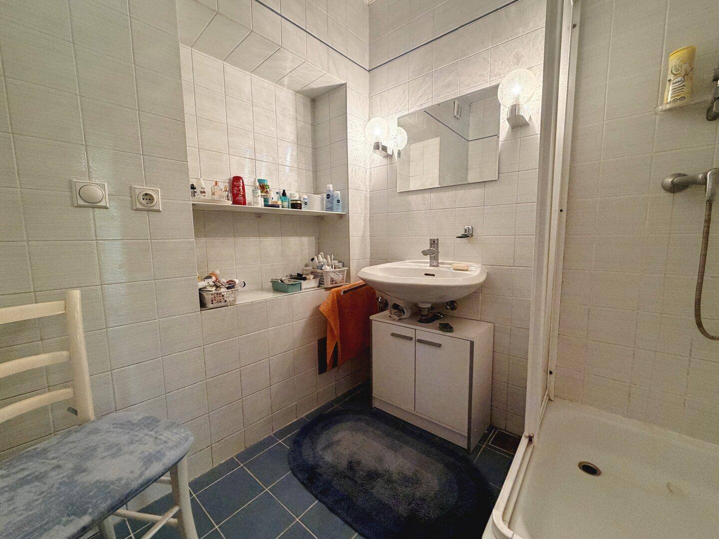 Kleines Badezimmer mit hellblauen Fliesen, Waschbecken und Duschbereich.