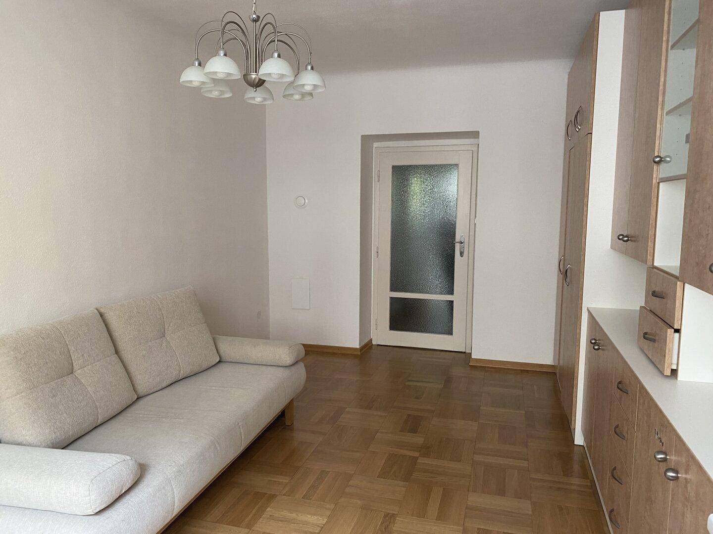 Gemütlicher Wohnbereich mit beigem Sofa, praktischen Einbauschränken und einer Tür zum Flur.