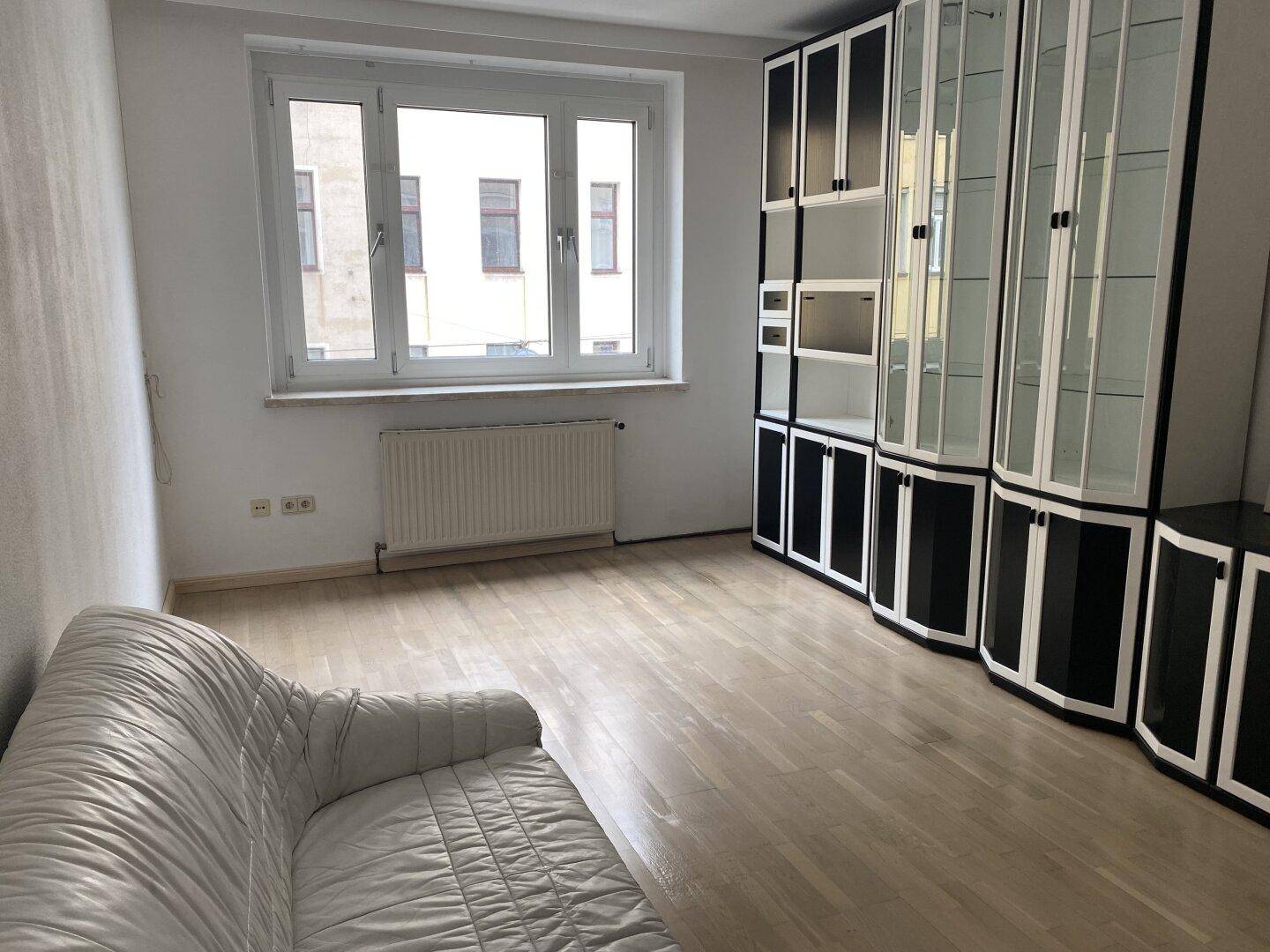 Wohnzimmer mit weißem Sofa, großer schwarz-weißer Schrankwand und Fenster mit Blick nach draußen.