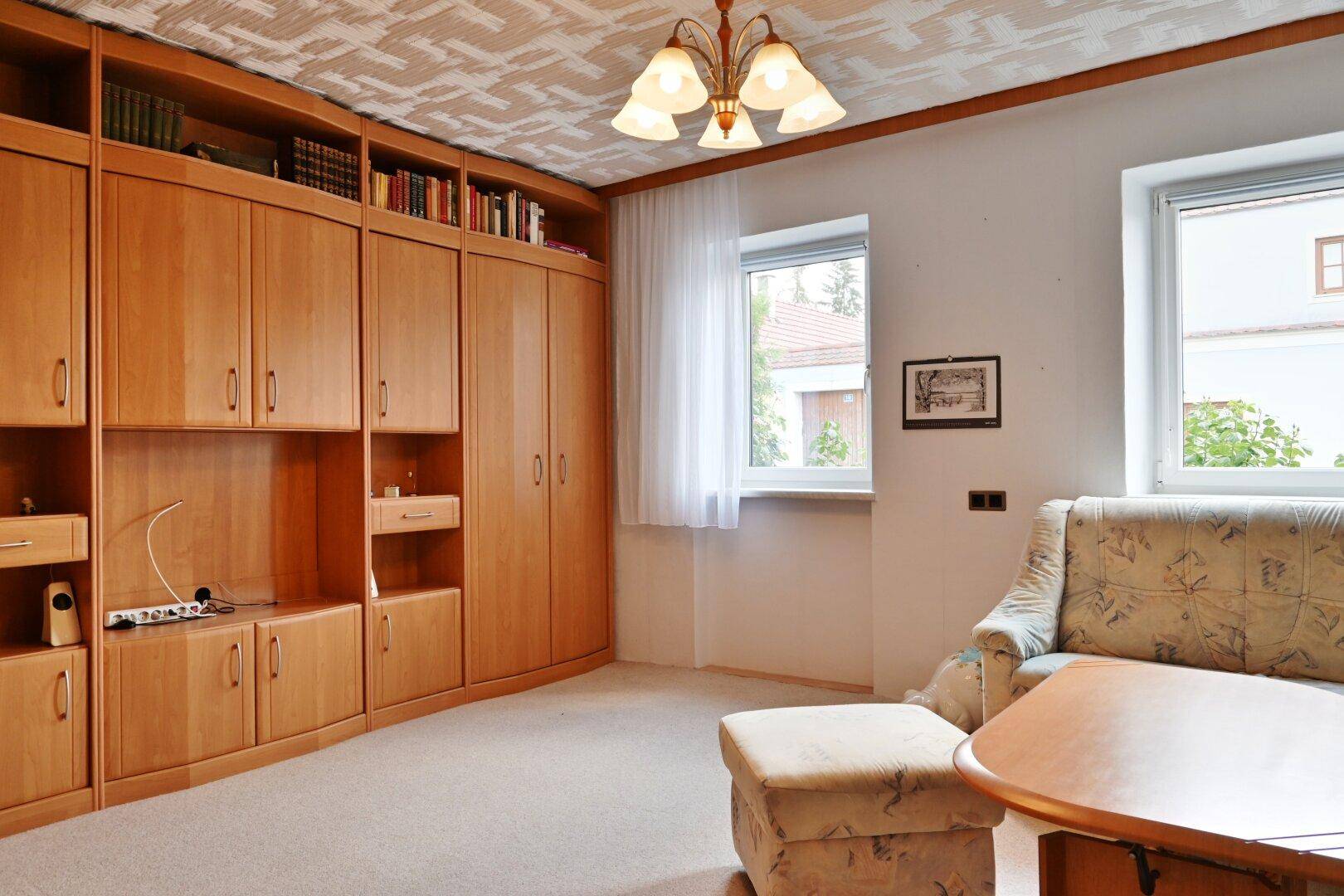 Wohnzimmer mit großem Holzschrank, Teppichboden und Blick auf die Umgebung.