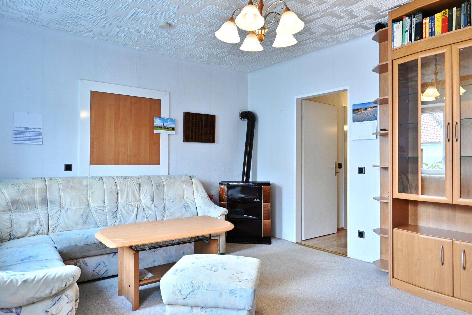 Gemütliches Wohnzimmer mit Kachelofen, Teppichboden und traditioneller Deckenverkleidung.